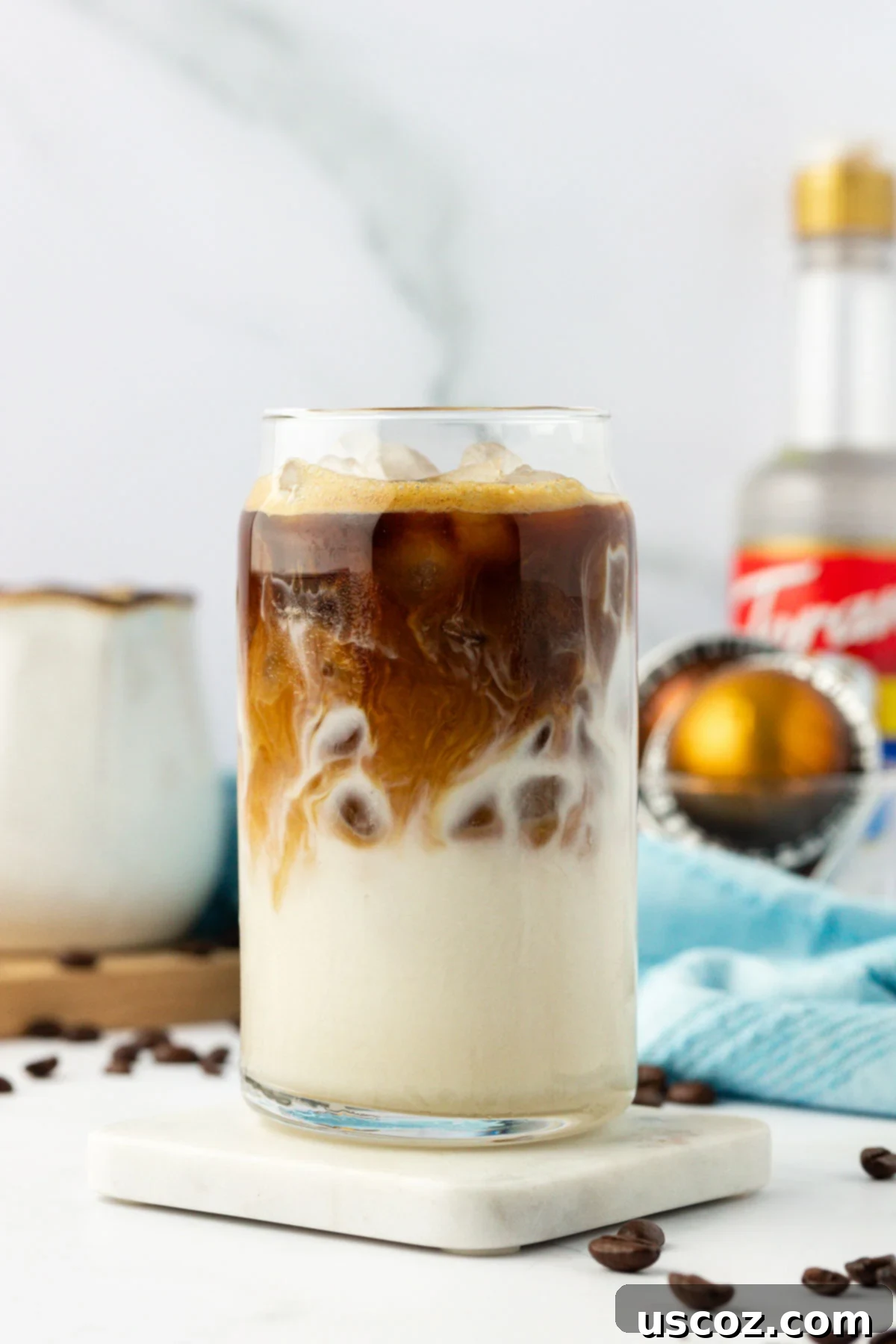 Silky Cold Espresso 2 A refreshing iced latte in a clear glass, showing distinct layers of milk, coffee, and ice. The condensation on the glass hints at its cool temperature, inviting a delicious sip.