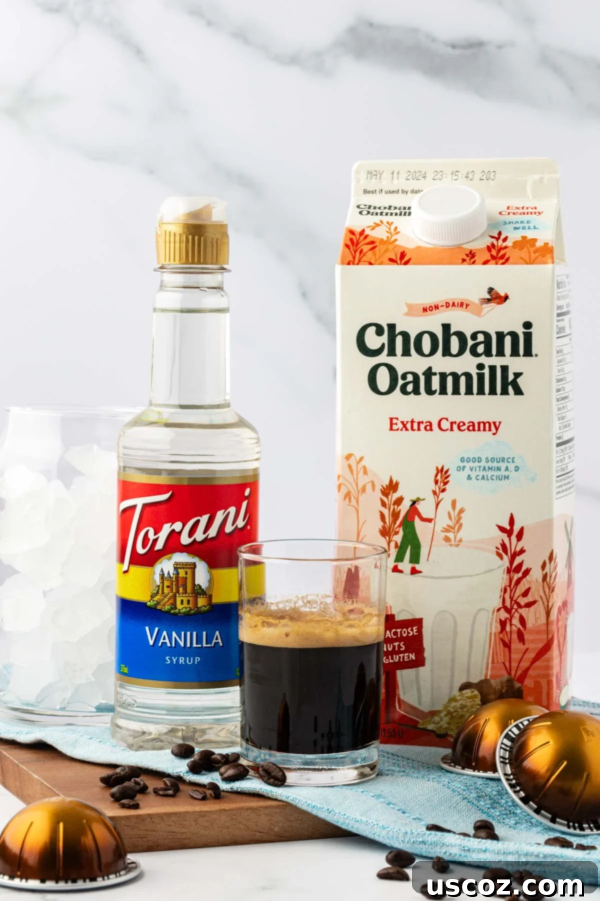 Silky Cold Espresso 3 Three essential ingredients for an iced latte: a bottle of oat milk, a small cup of rich espresso, and a bottle of vanilla syrup, all ready for mixing.