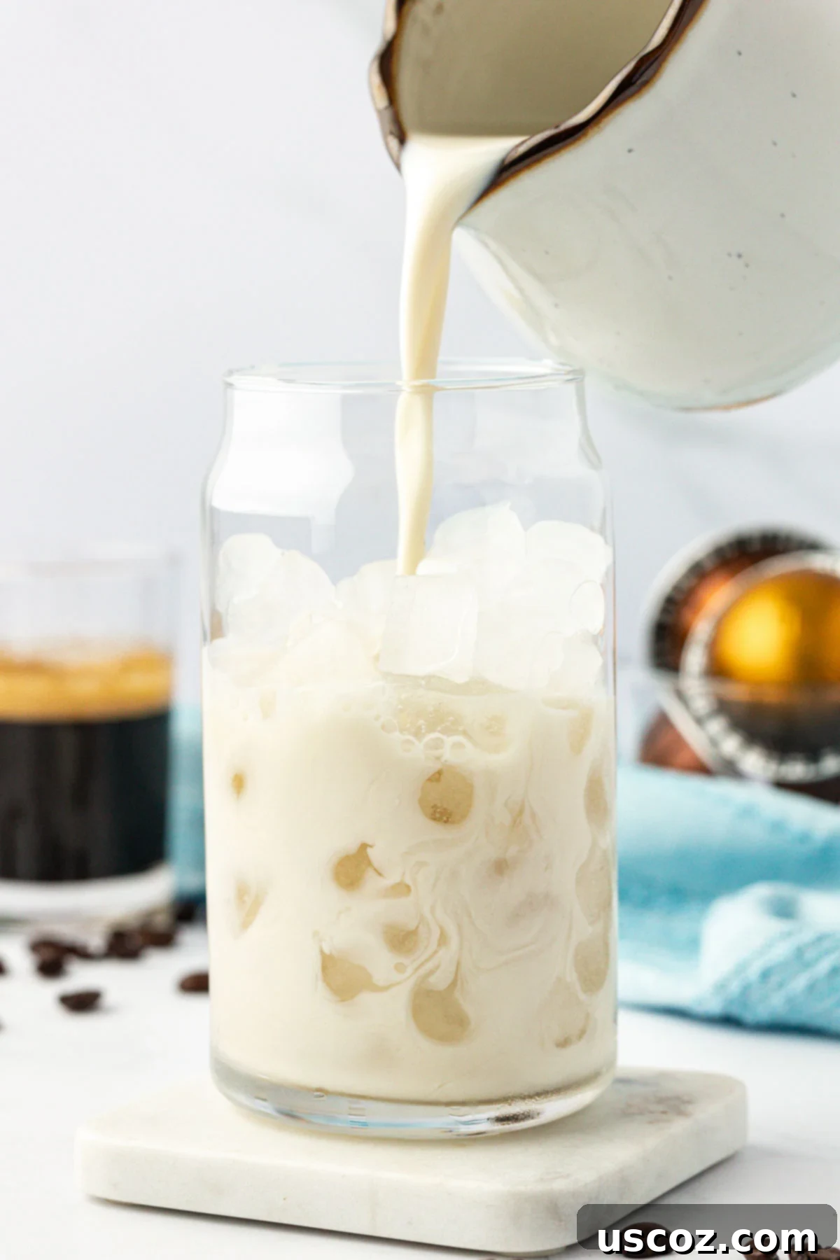 Silky Cold Espresso 4 Pouring creamy oat milk into a clear glass already filled with glistening ice cubes, preparing the base for an iced latte.