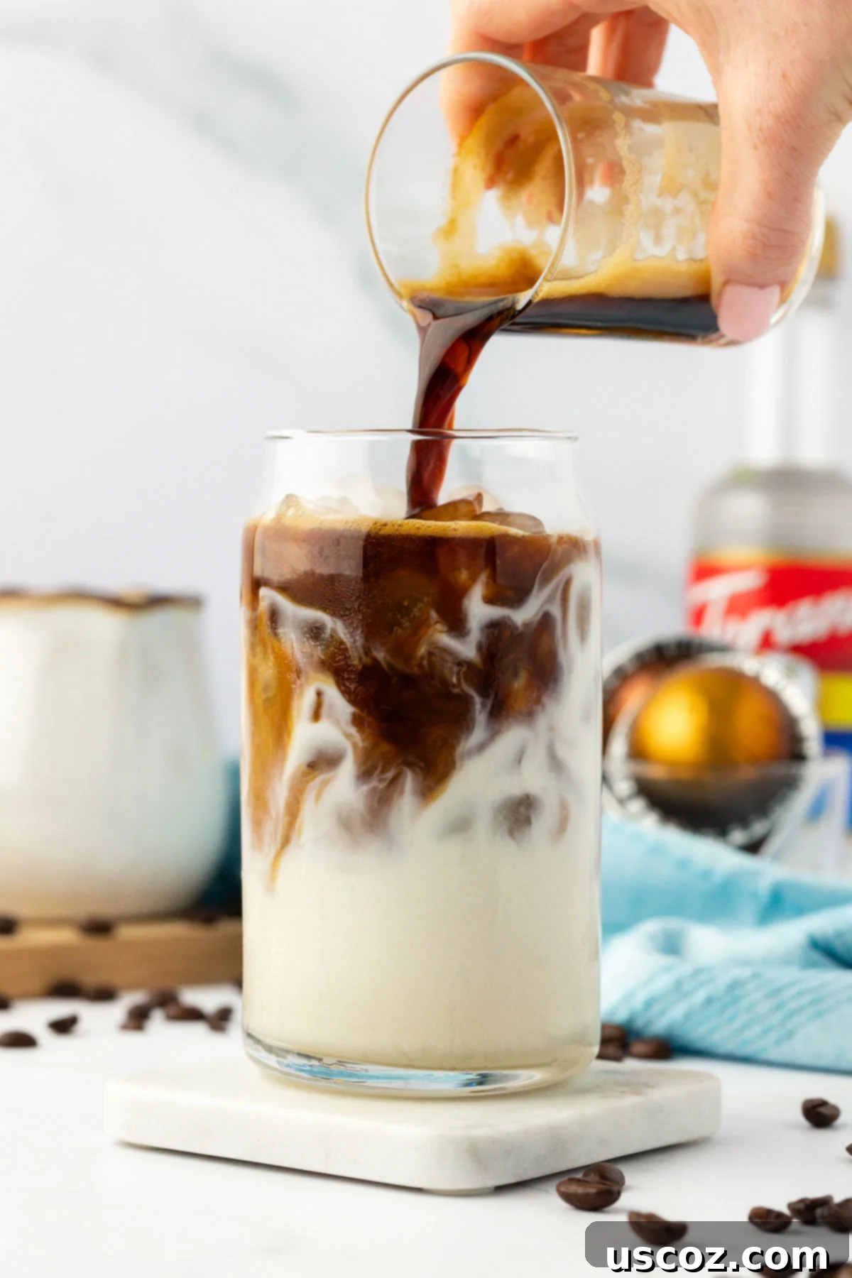 Silky Cold Espresso 7 A vibrant stream of dark espresso being poured over a glass of white milk and ice, creating beautiful swirls and layers for an iced latte.