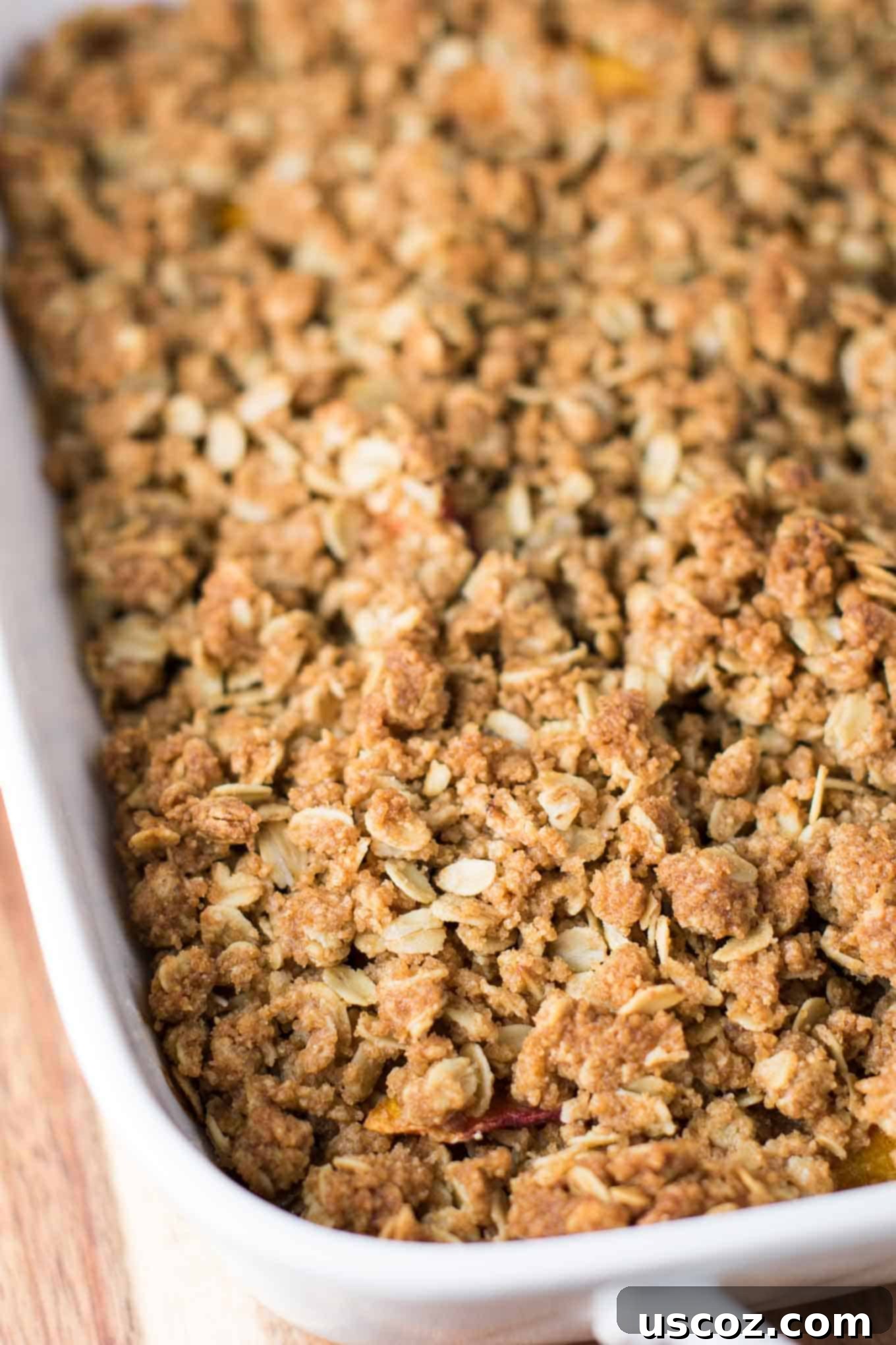 Delicious & Easy Peach Crisp 5 Spoon oat crisp topping evenly over the peach filling in a baking dish