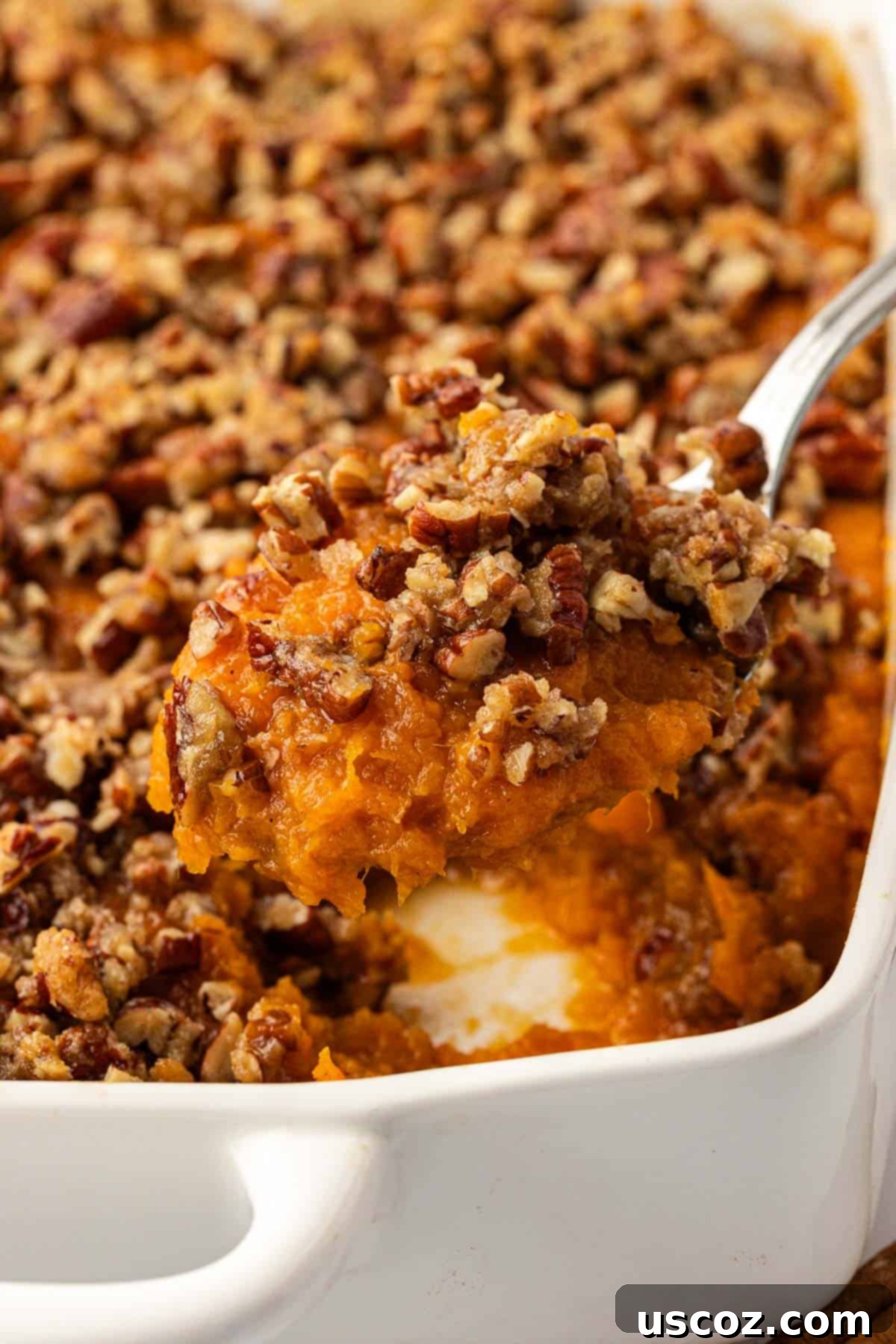 Golden Sweet Potato & Pecan Delight 3 A serving spoon lifting a generous scoop of fluffy sweet potato casserole with visible, golden pecan topping from a large baking dish.