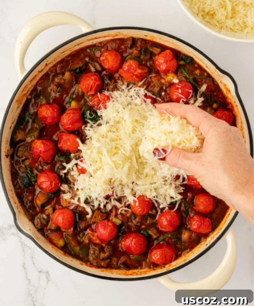 adding mozzarella and parmesan cheese to the pasta sauce