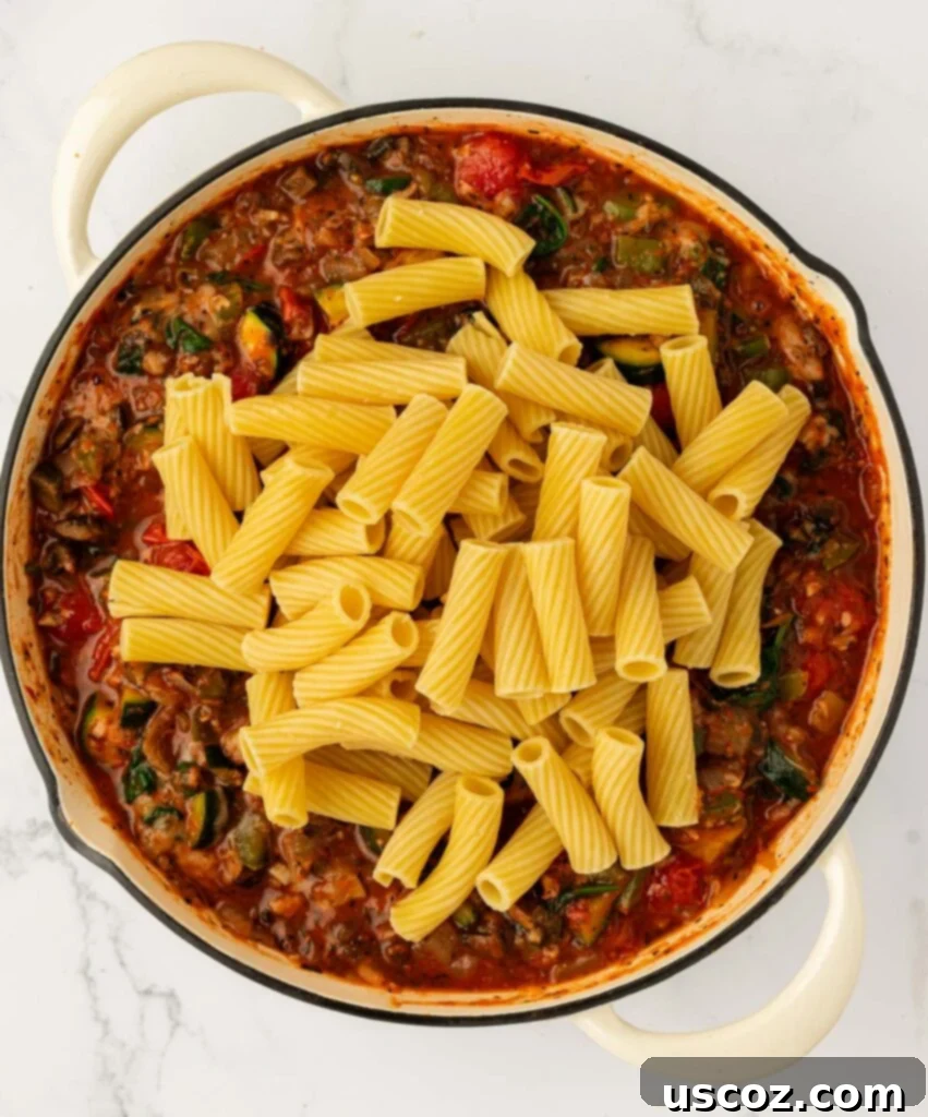 adding cooked rigatoni noodles to the vegetable pasta sauce