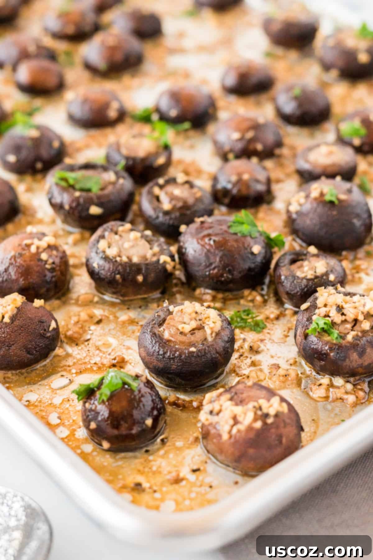 Garlicky Roasted Mushrooms 3 mushrooms roasted in garlic butter on a baking sheet, glistening with butter