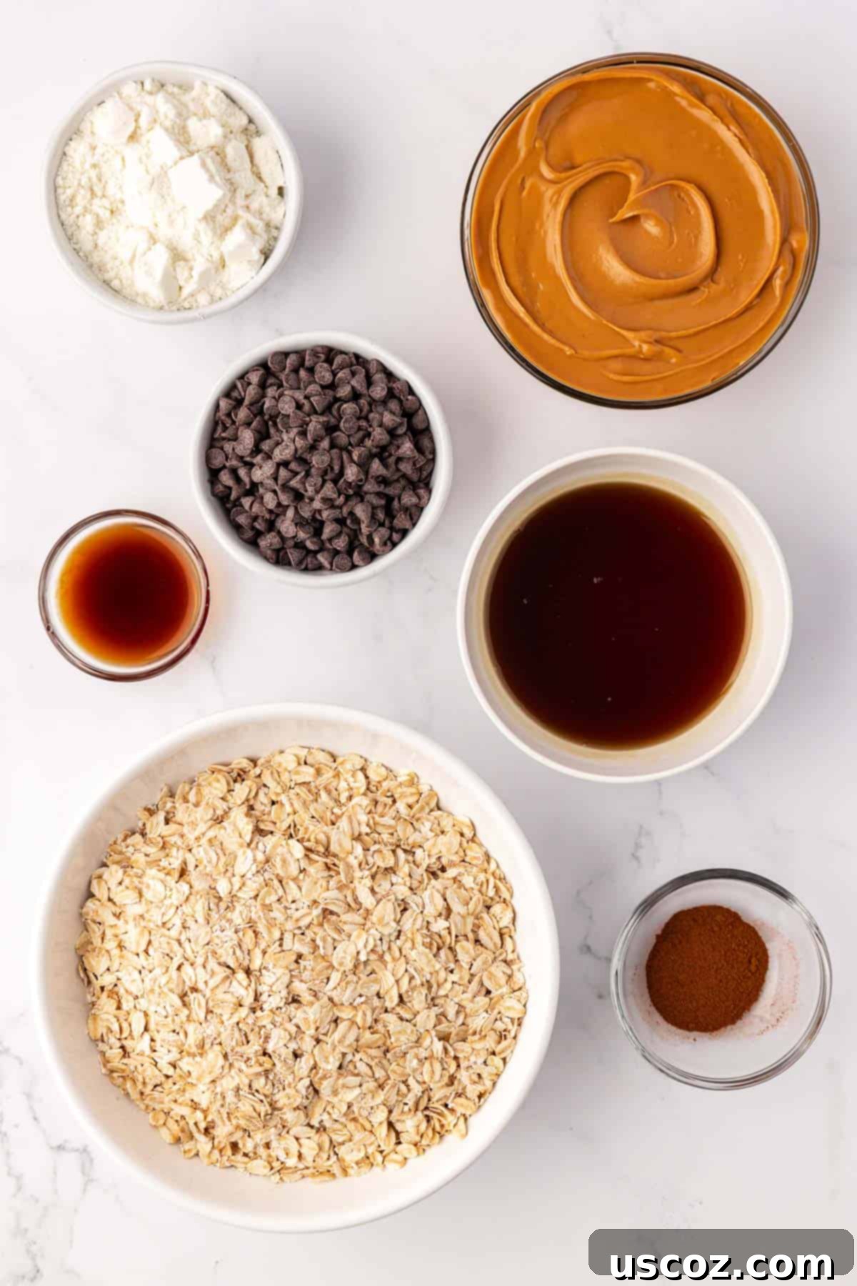 Oat Cookie Power Bites 4 Individual ingredients for oatmeal cookie energy bites laid out on a clean counter: peanut butter, maple syrup, oats, protein powder, chocolate chips, cinnamon, and vanilla extract.