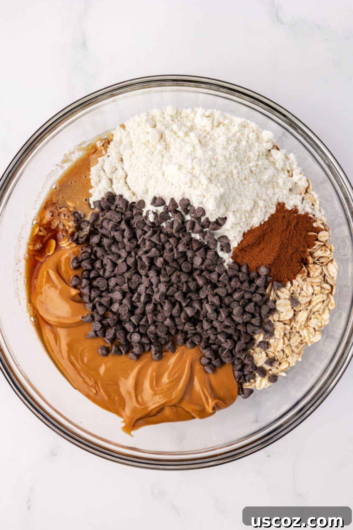 Oat Cookie Power Bites 5 All the dry and wet ingredients for energy balls, including oats, peanut butter, and chocolate chips, in a large mixing bowl before mixing.