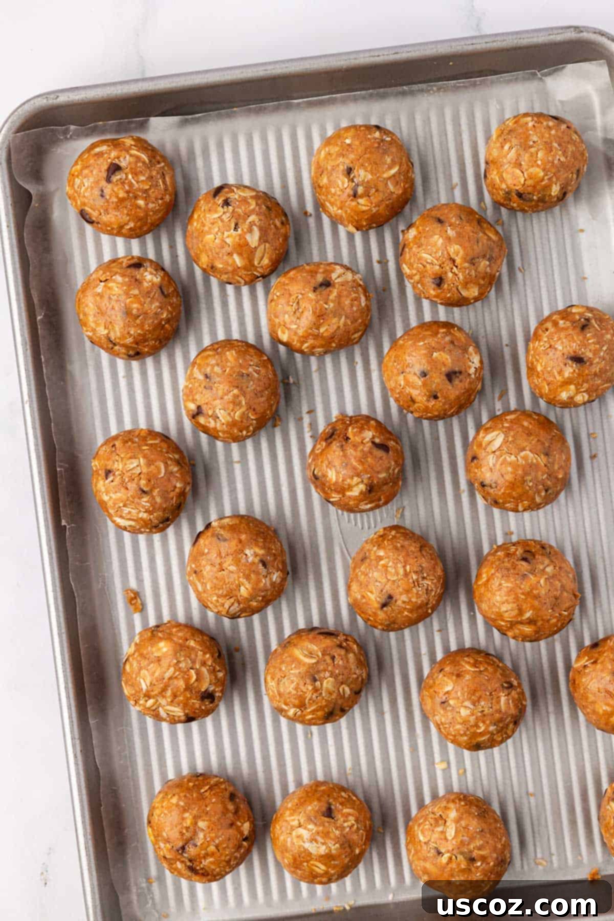 Oat Cookie Power Bites 7 Freshly scooped and rolled oatmeal cookie energy balls arranged neatly on a wax paper-lined baking sheet, ready for chilling.