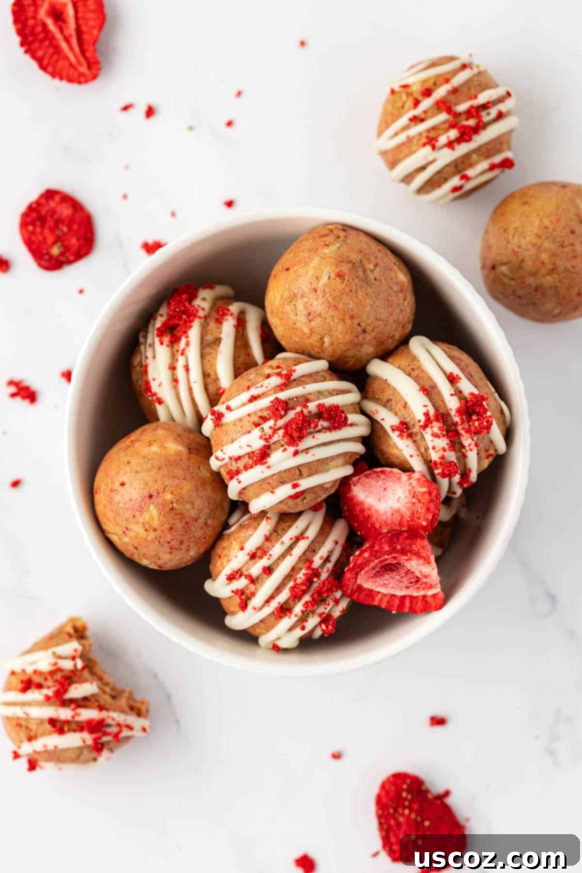 Strawberry Cream Energy Bites 2 strawberries and cream energy bites with white chocolate drizzle and strawberry powder