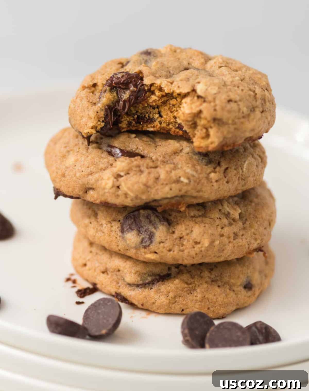 Wholesome Chocolate Chip Comforts 3 A stack of four whole wheat chocolate chip cookies on a white surface, with the top cookie having a bite taken out of it.