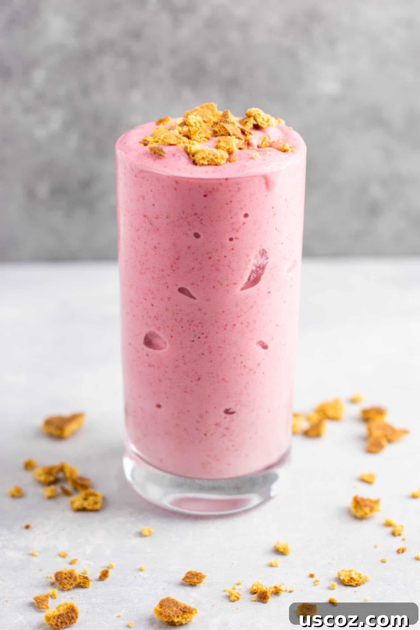 strawberry cheesecake smoothie in a glass with crushed graham cracker on top