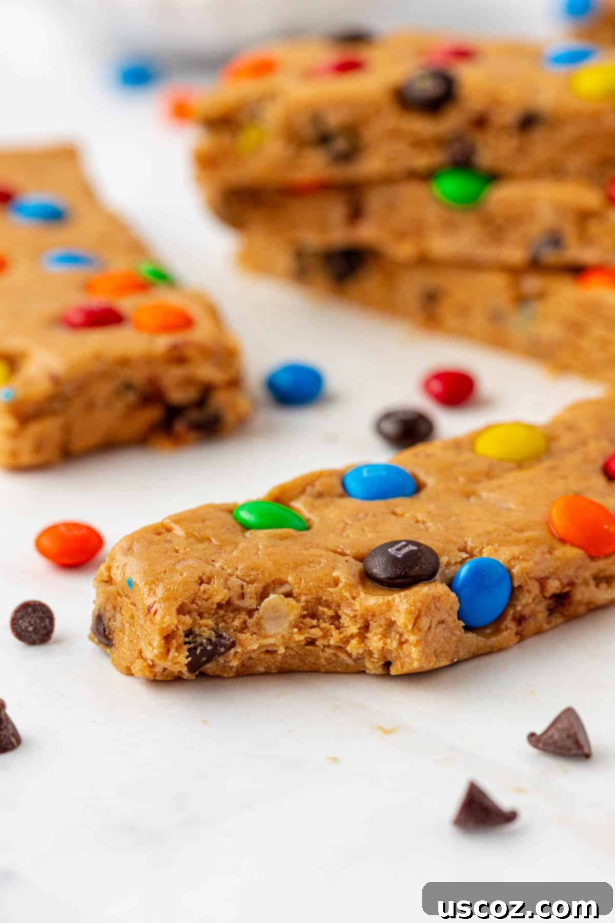 Monster Cookie Protein Bars 12 Stack of Monster Cookie Protein Bars on a wooden surface, with some M&Ms sprinkled around