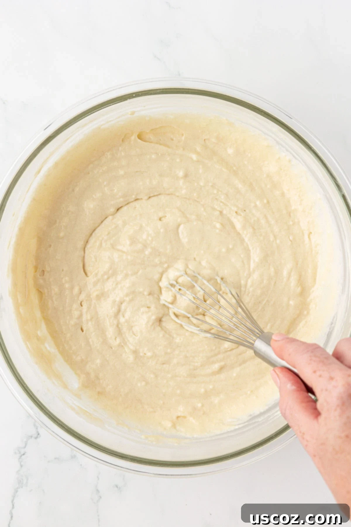 A rubber spatula gently mixing the Greek yogurt waffle batter, showing a perfectly combined, slightly lumpy consistency.