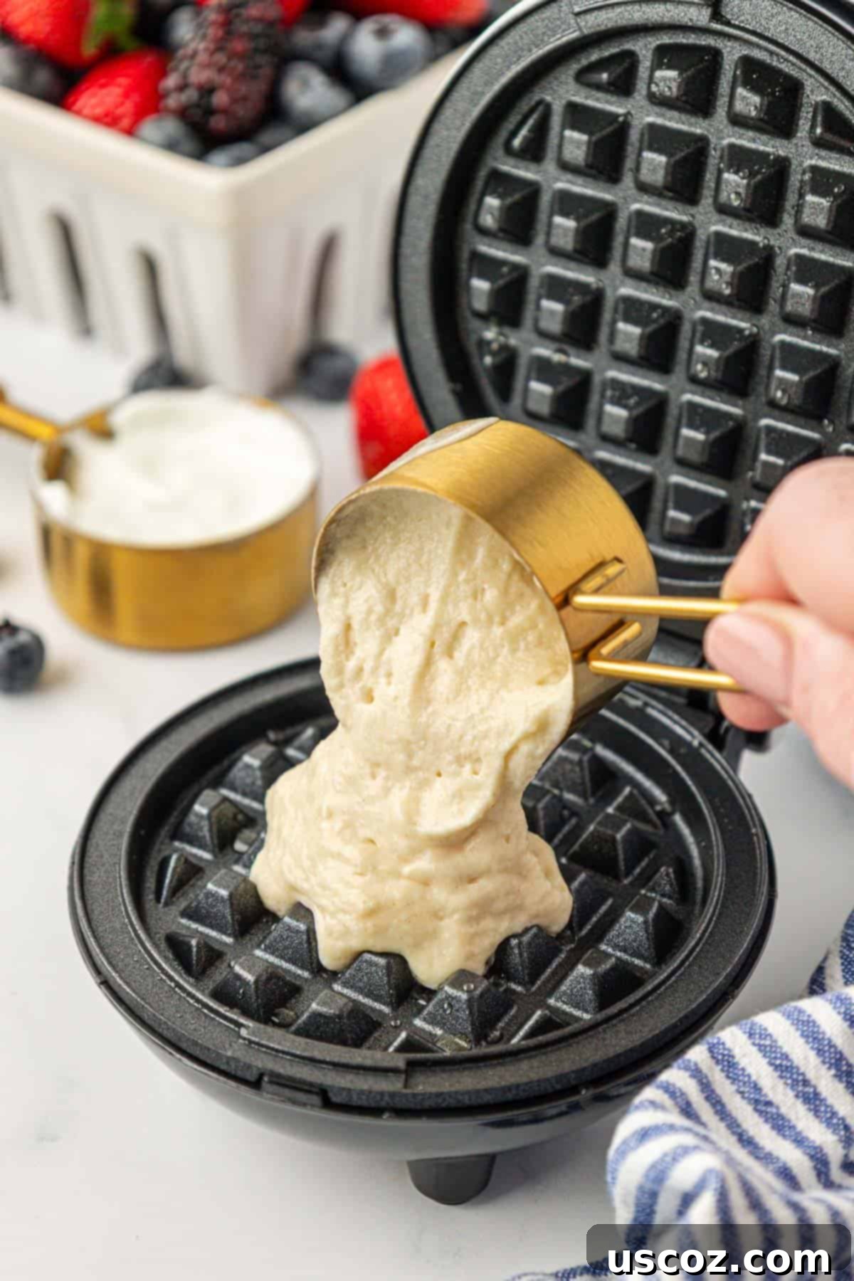 Pouring a measured amount of Greek yogurt waffle batter into a heated mini waffle maker.