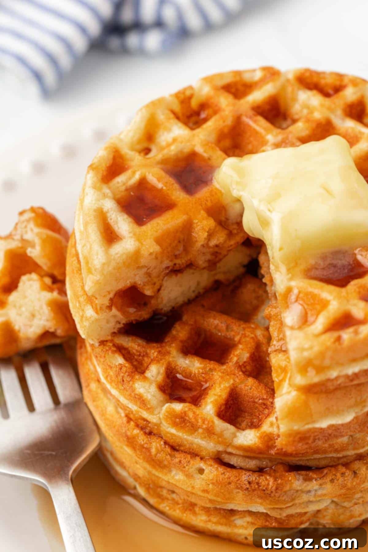 A stack of Greek yogurt waffles topped with a pat of melting butter and drizzled with golden syrup.