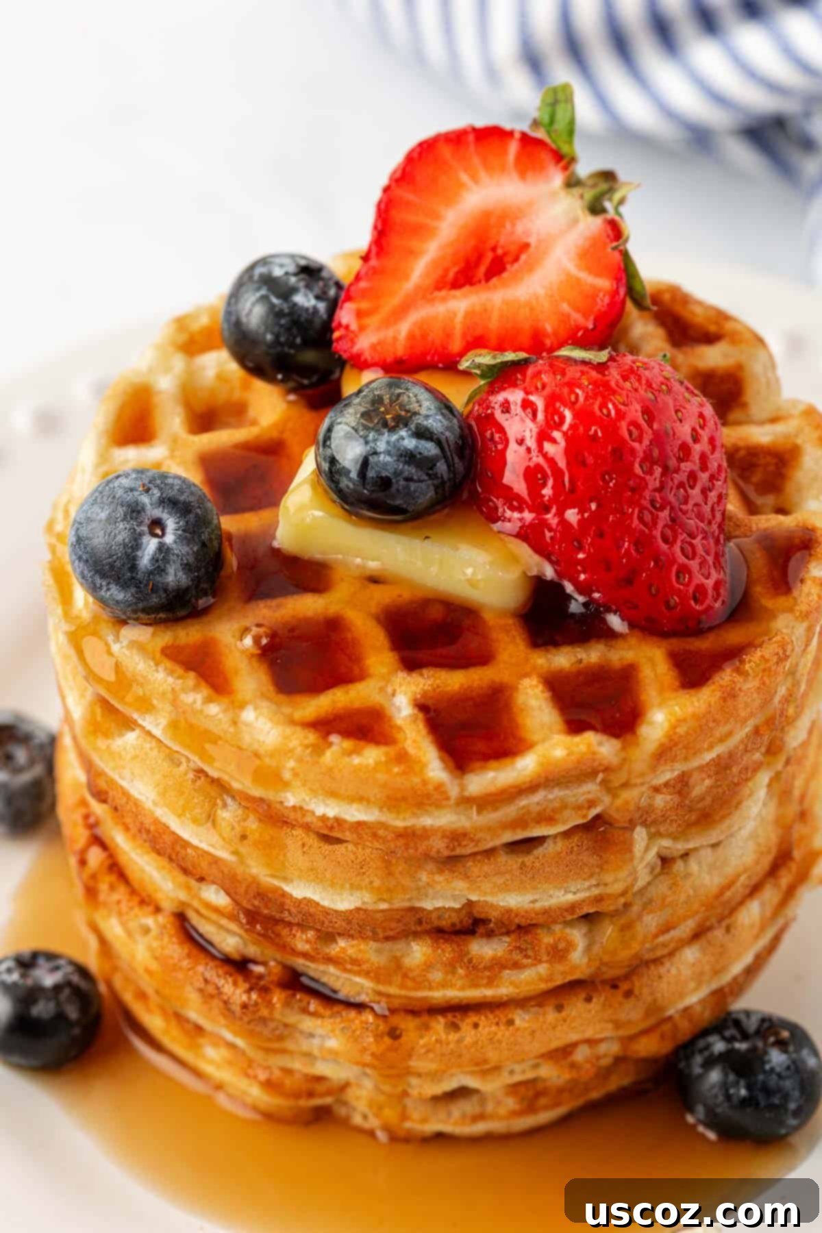 An appetizing overhead view of Greek yogurt waffles, generously topped with an assortment of fresh berries, a drizzle of syrup, and a dollop of butter.