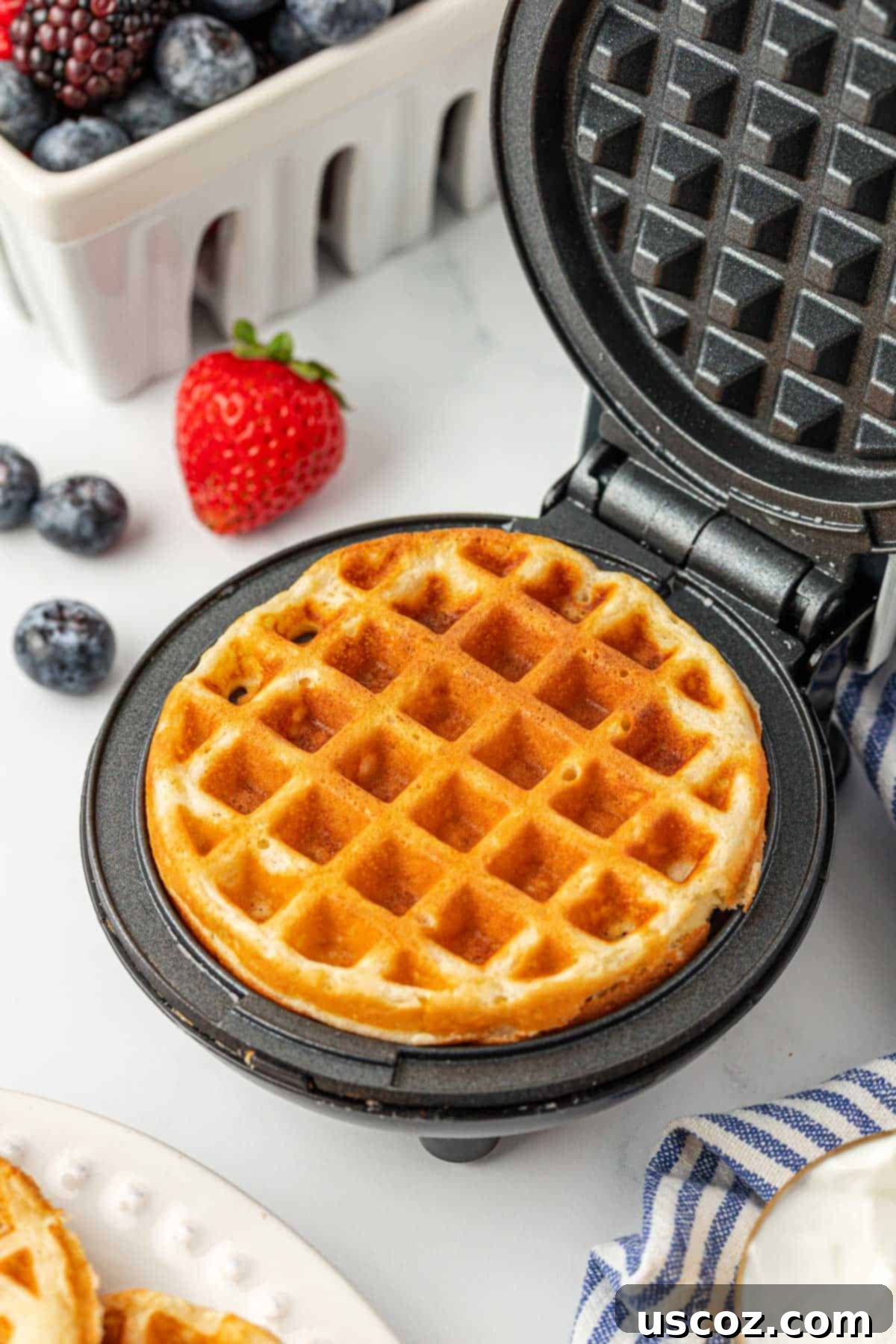 A freshly cooked mini Greek yogurt waffle being removed from a bright red Dash mini waffle maker, showing its perfectly golden texture.