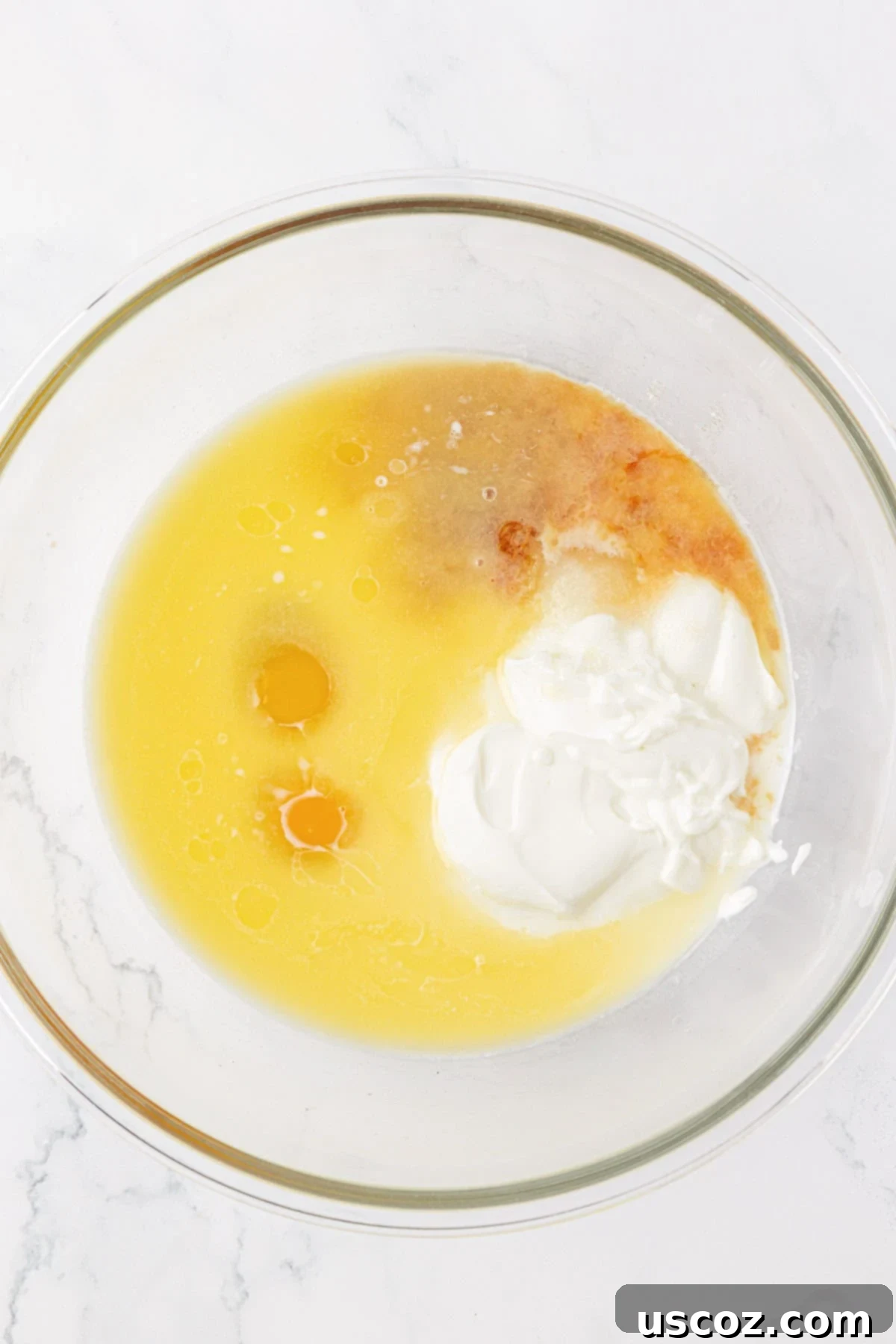 A bowl containing wet ingredients for waffle batter: sugar, Greek yogurt, milk, melted butter, eggs, and vanilla extract.
