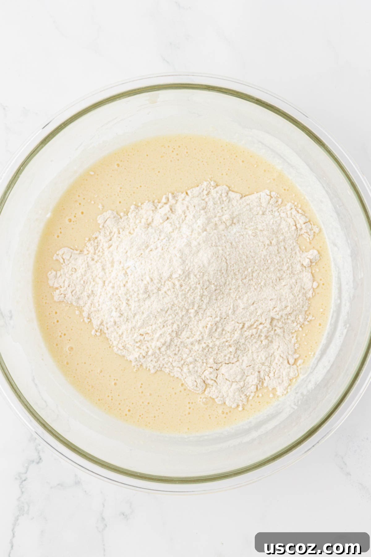 Pouring the whisked wet ingredients into the bowl of dry ingredients for the waffle batter.