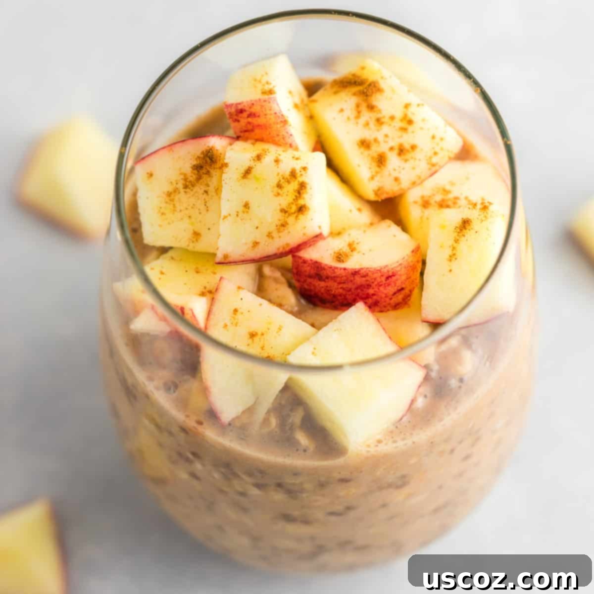 Apple Cinnamon Overnight Oats 2 A glass jar filled with creamy apple cinnamon overnight oats, topped generously with diced fresh red apples and a sprinkle of cinnamon powder.