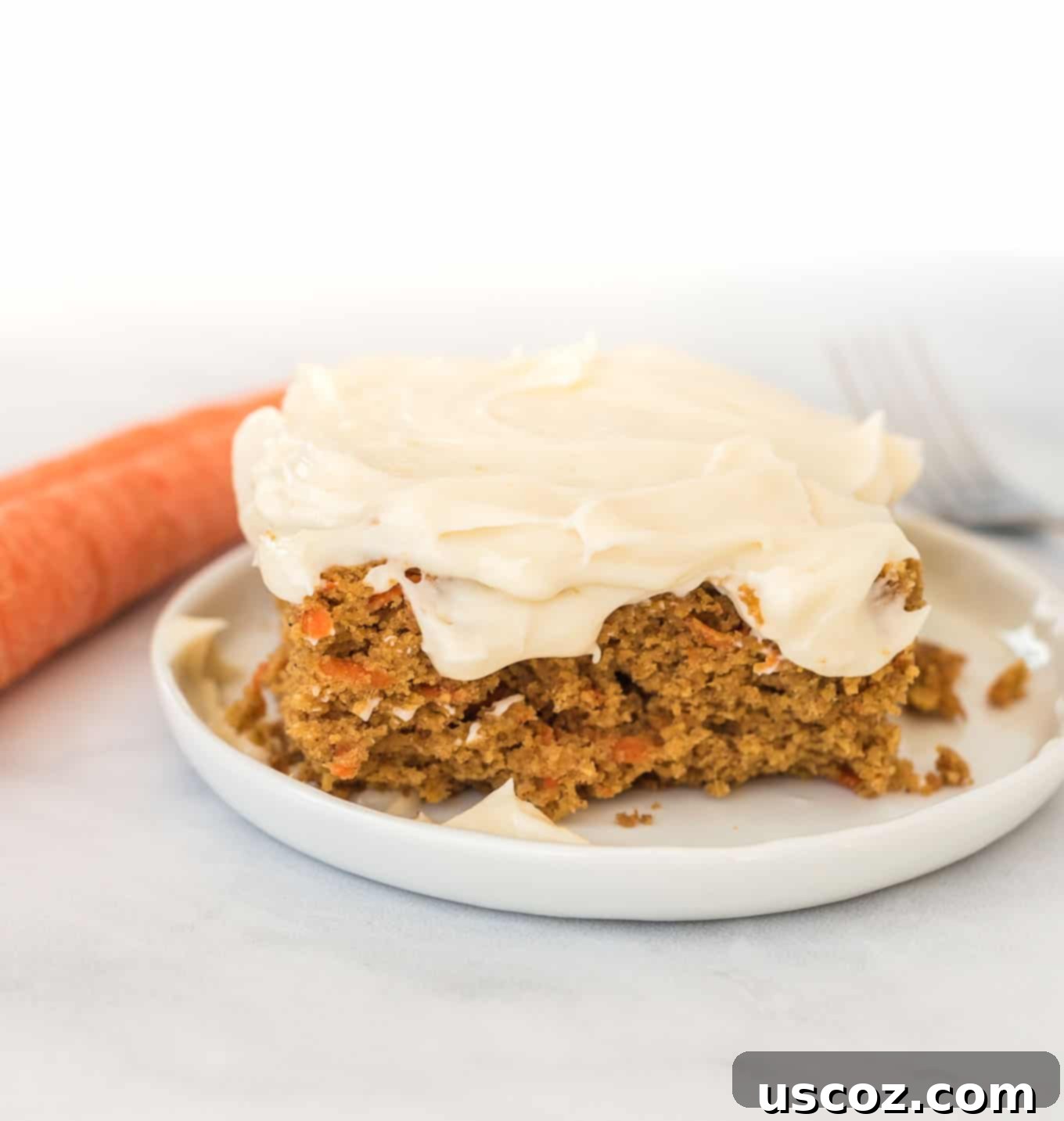 Gluten-Free Carrot Cake Perfection 8 A pristine slice of gluten-free carrot cake, topped with a generous dollop of smooth cream cheese frosting, on a simple white plate.