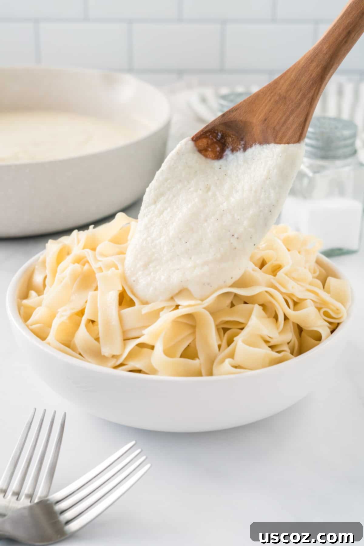Creamy Cauliflower Alfredo 13 pouring cauliflower Alfredo sauce over a bowl of fettuccini noodles