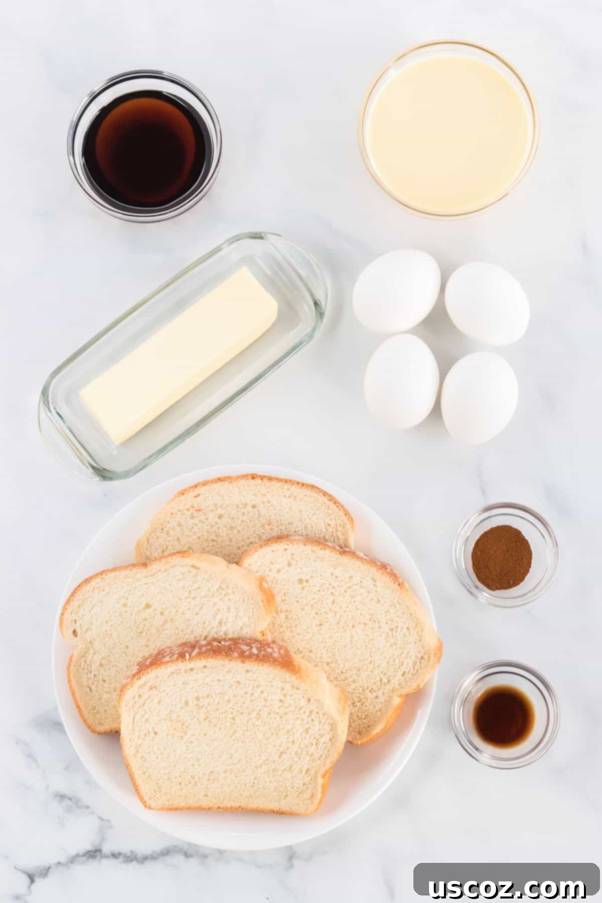 Festive Eggnog French Toast 3 Various ingredients laid out for making eggnog french toast including eggs, eggnog, bread, vanilla, cinnamon, and butter on a rustic wooden board