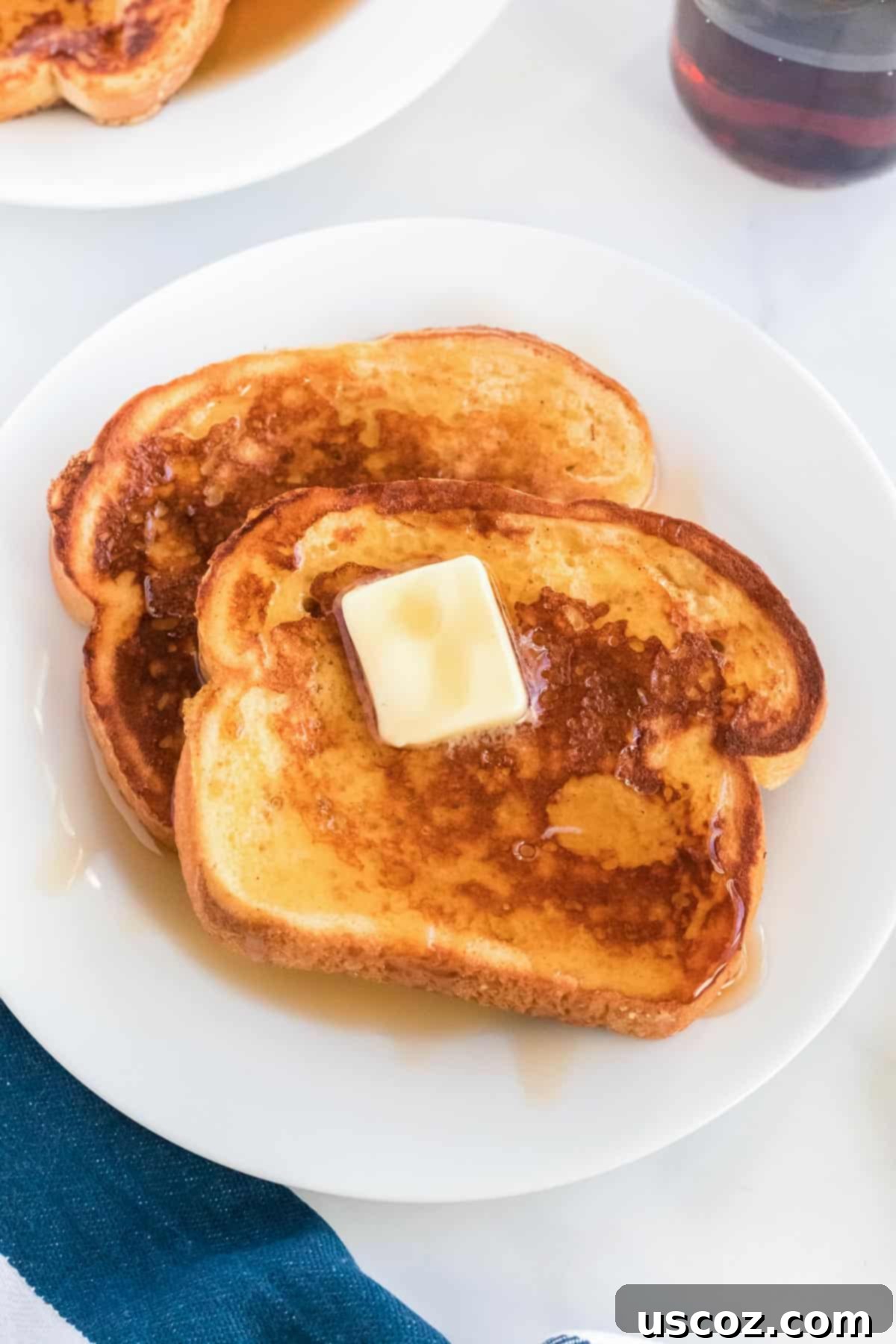 Festive Eggnog French Toast 8 Close-up of golden Eggnog French Toast slices on a plate with melted butter and rich maple syrup, ready for a delicious holiday meal