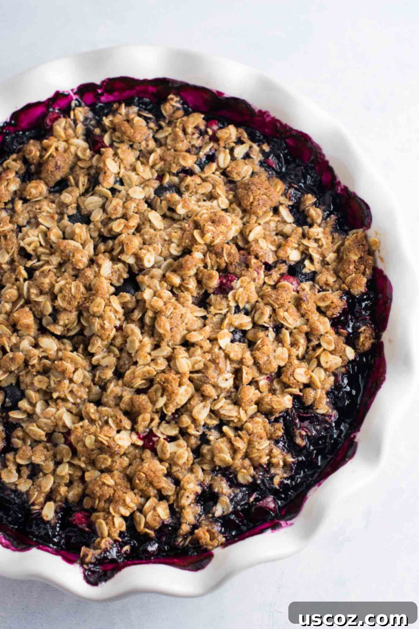Sweet Tart Cranberry Blueberry Crisp 4 Cranberry blueberry crisp being assembled in a pie dish, with the fruit filling at the bottom and the crumb topping ready to be spread.