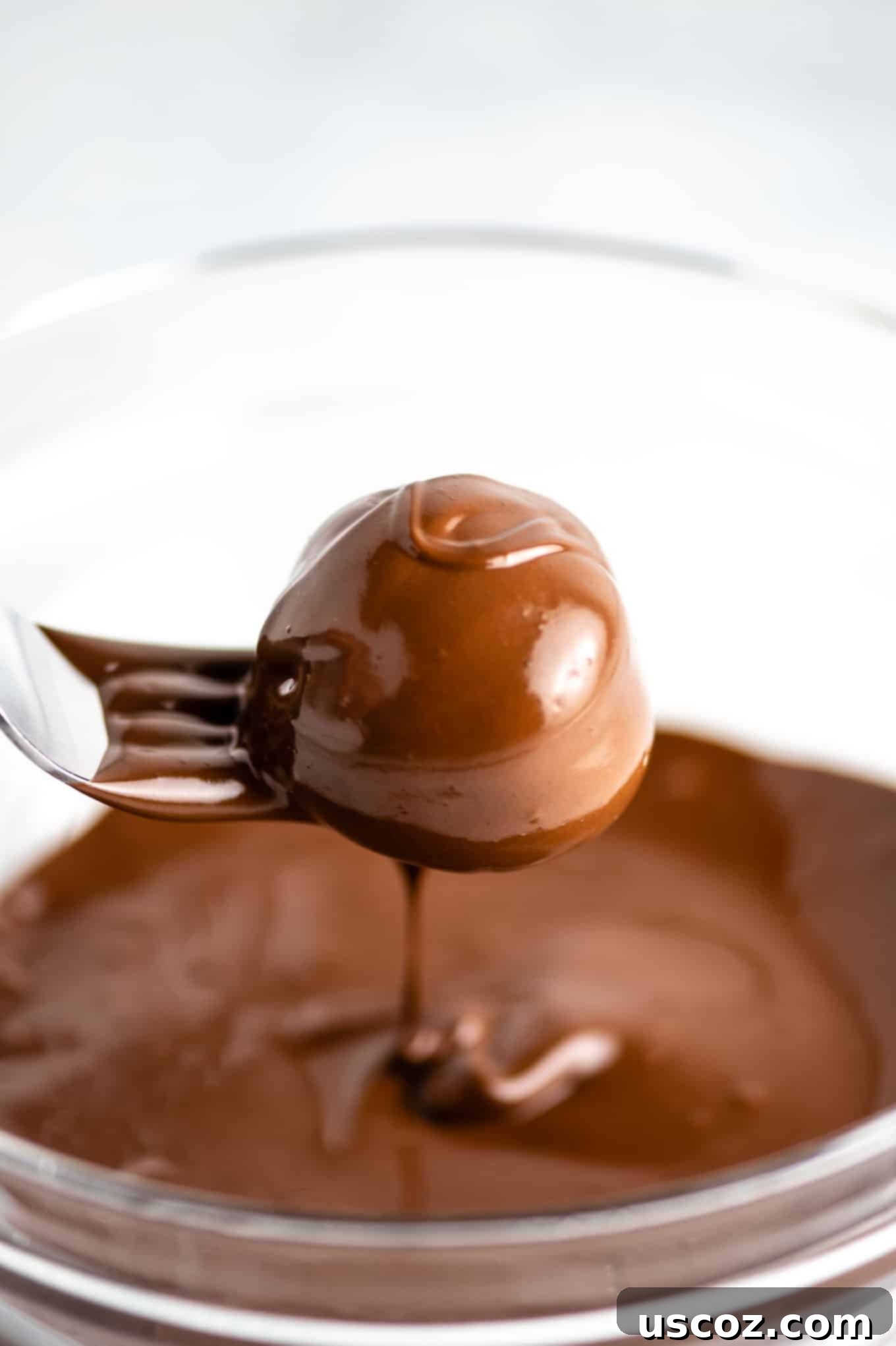 Decadent Yet Healthy No-Bake Peanut Butter Truffles 6 A peanut butter truffle being dipped into a bowl of melted chocolate with a spoon.