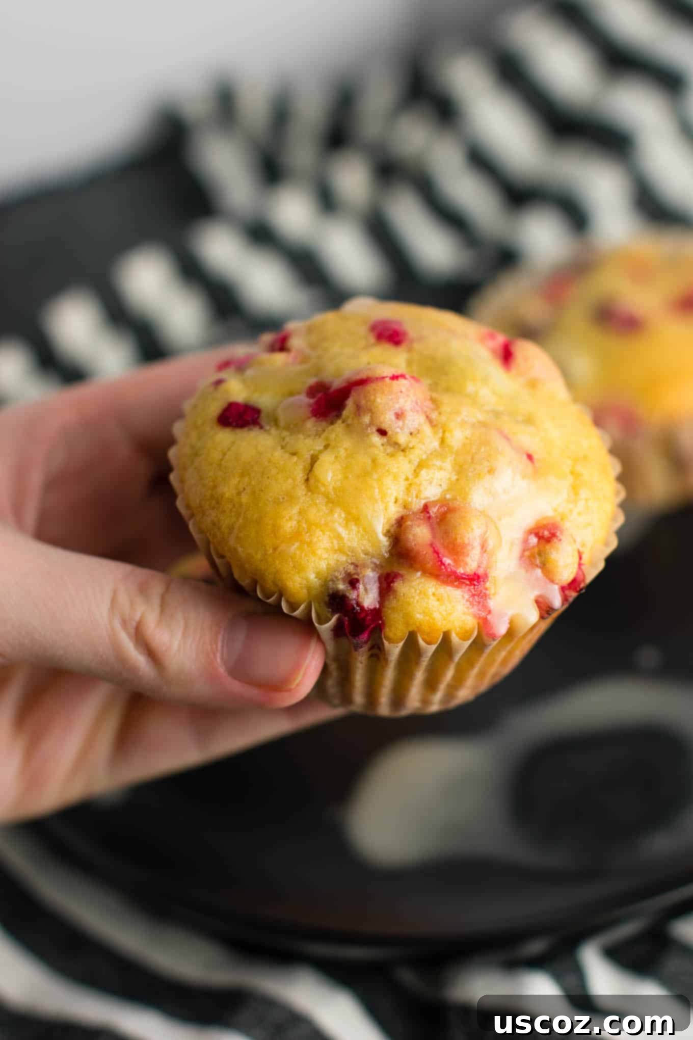 Wholesome Cranberry Orange Muffins 7 A stack of three healthy cranberry orange muffins on a white plate, with the orange glaze visible.