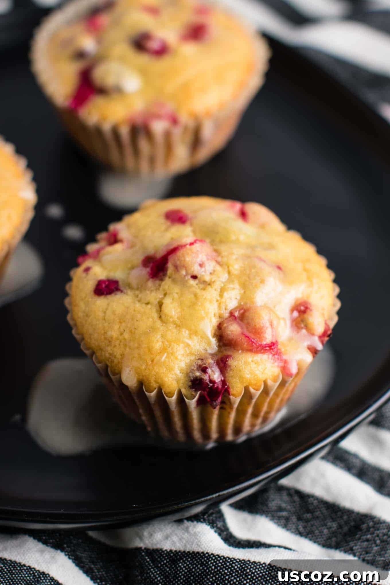 Wholesome Cranberry Orange Muffins 8 Three healthy cranberry orange muffins with orange glaze on a wooden cutting board.