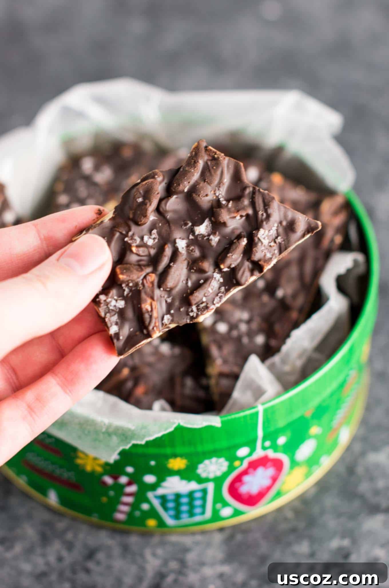 Decadent Dark Chocolate Almond Bark 9 A hand delicately holding a perfectly broken piece of dark chocolate almond bark, showcasing its inviting texture.