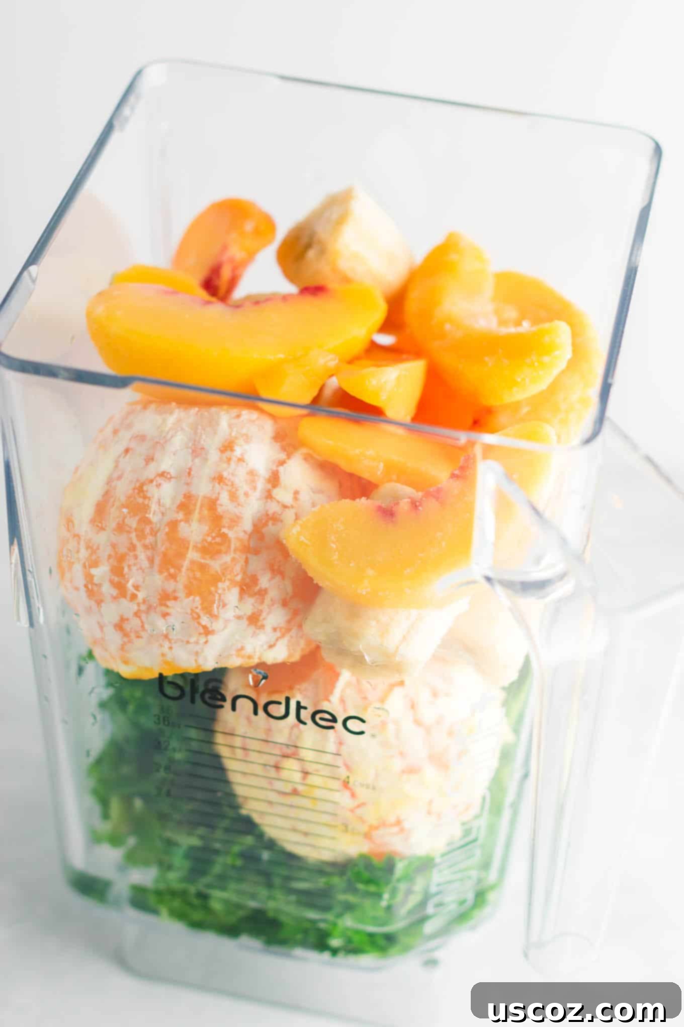 Vibrant Citrus Kale Green Smoothie 4 blender with kale, oranges, frozen peaches, and frozen bananas in it