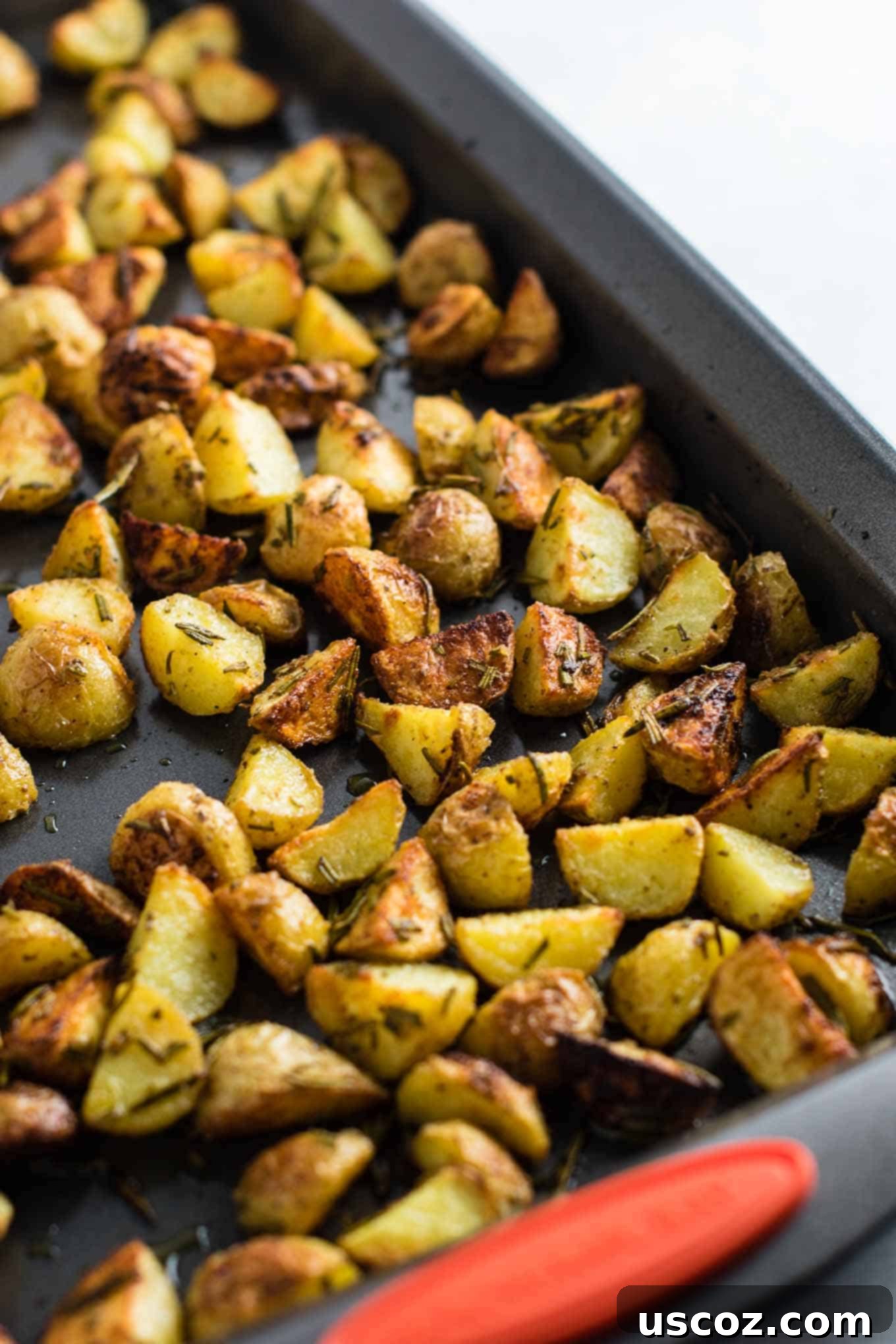 A metal spatula carefully turning and stirring the partially roasted potatoes on a baking sheet, showcasing their developing golden-brown texture.