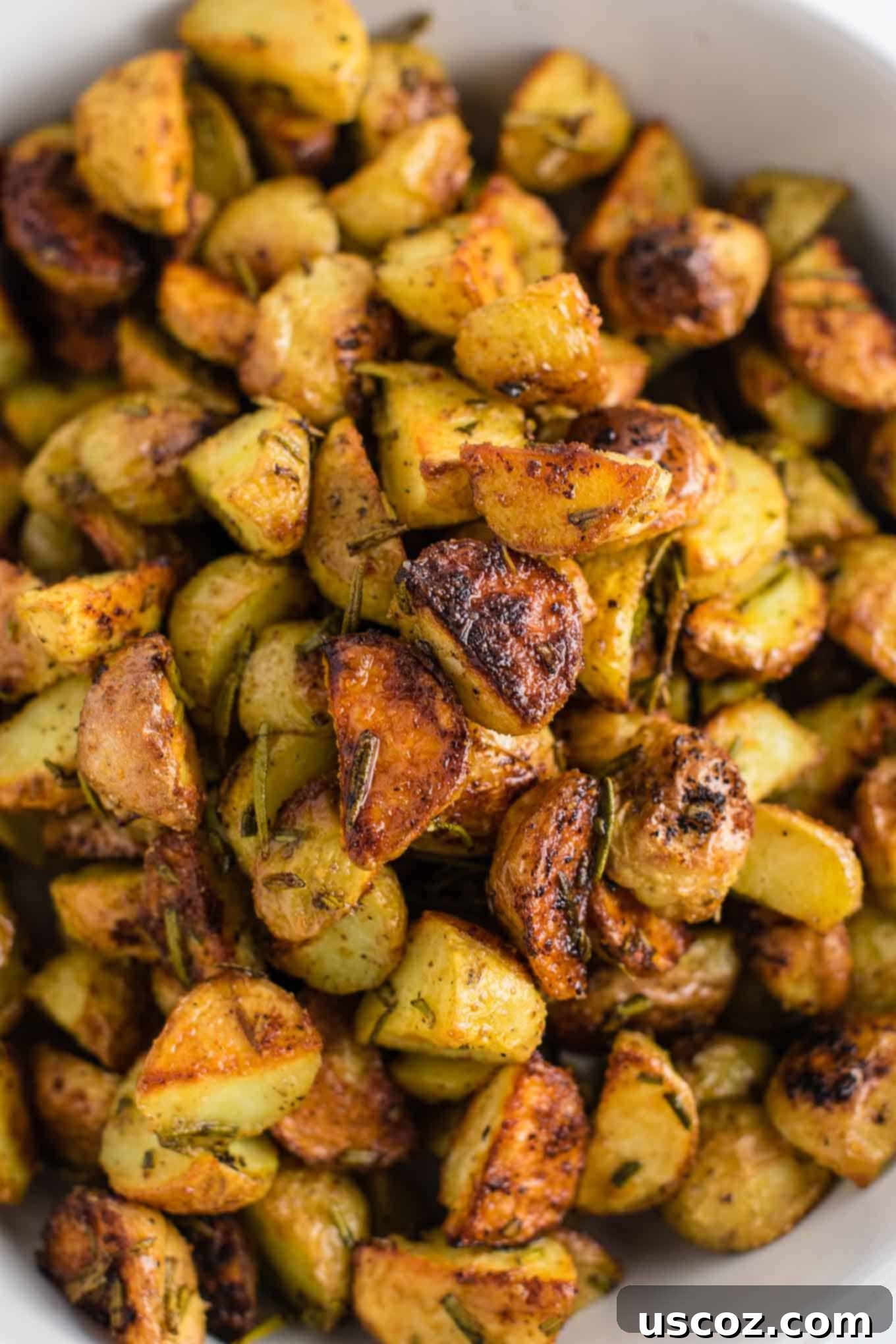 A close-up view of a baking sheet overflowing with perfectly golden-brown and crispy rosemary roasted potatoes, fresh out of the oven.