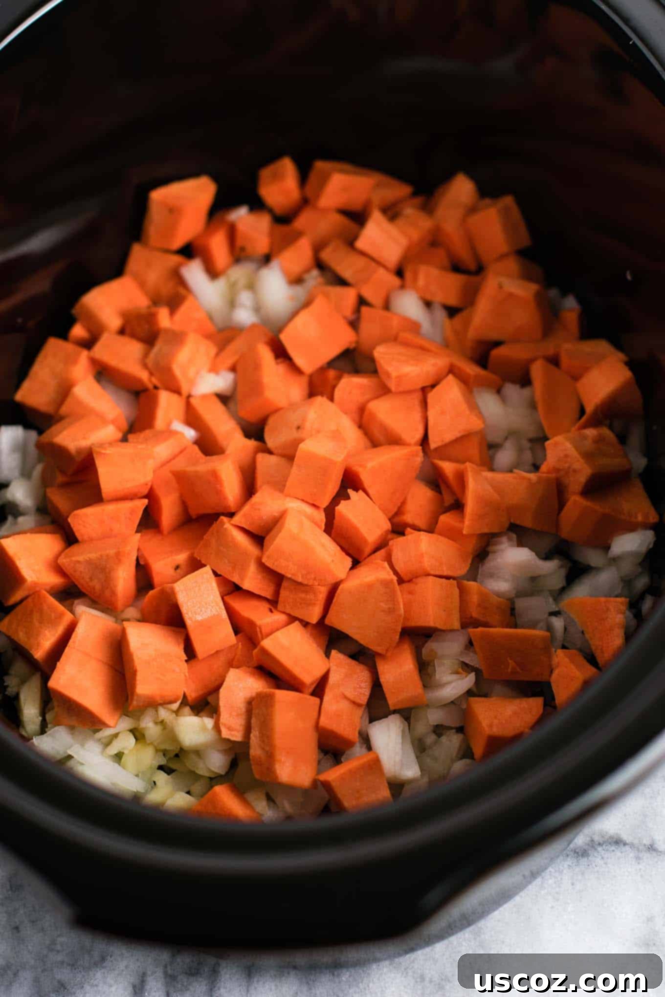 Easy Slow Cooker Vegetarian Sweet Potato Chili 4 A close-up shot of the raw ingredients for slow cooker vegetarian sweet potato chili in a crockpot, showcasing diced sweet potatoes, onions, and garlic.