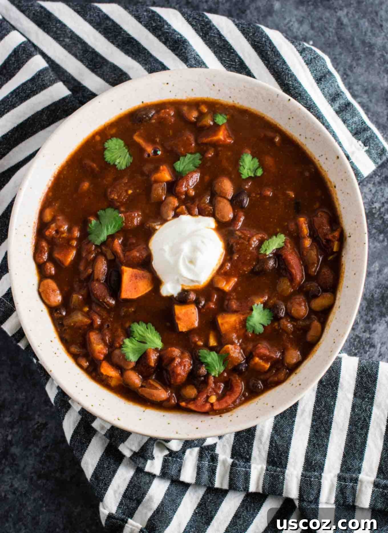 Easy Slow Cooker Vegetarian Sweet Potato Chili 7 A serving of Slow Cooker Vegetarian Sweet Potato Chili in a bowl, garnished with sour cream, shredded cheese, and fresh cilantro, on a wooden table.