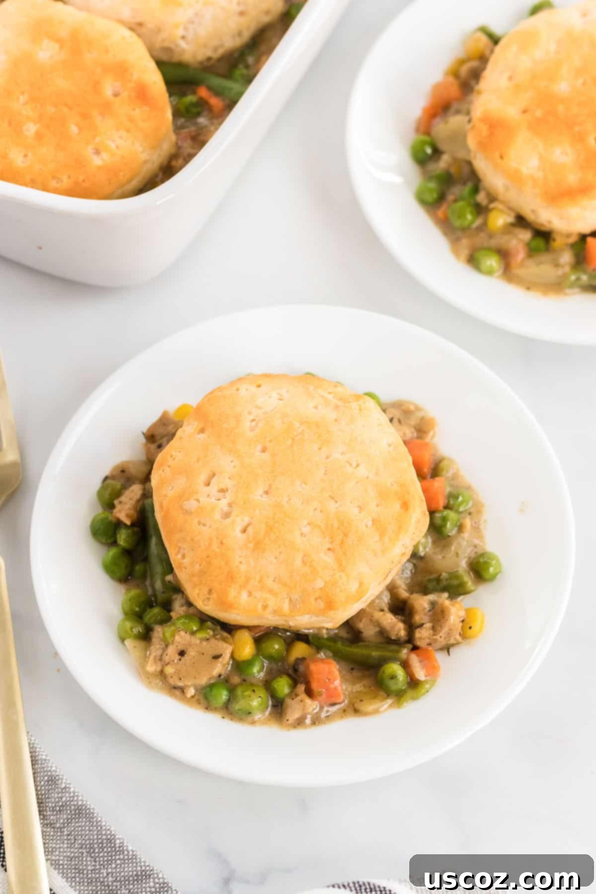 Garden Harvest Pie 12 A single serving of veggie pot pie topped with a golden biscuit, placed on a white plate with a fork, ready to be enjoyed.