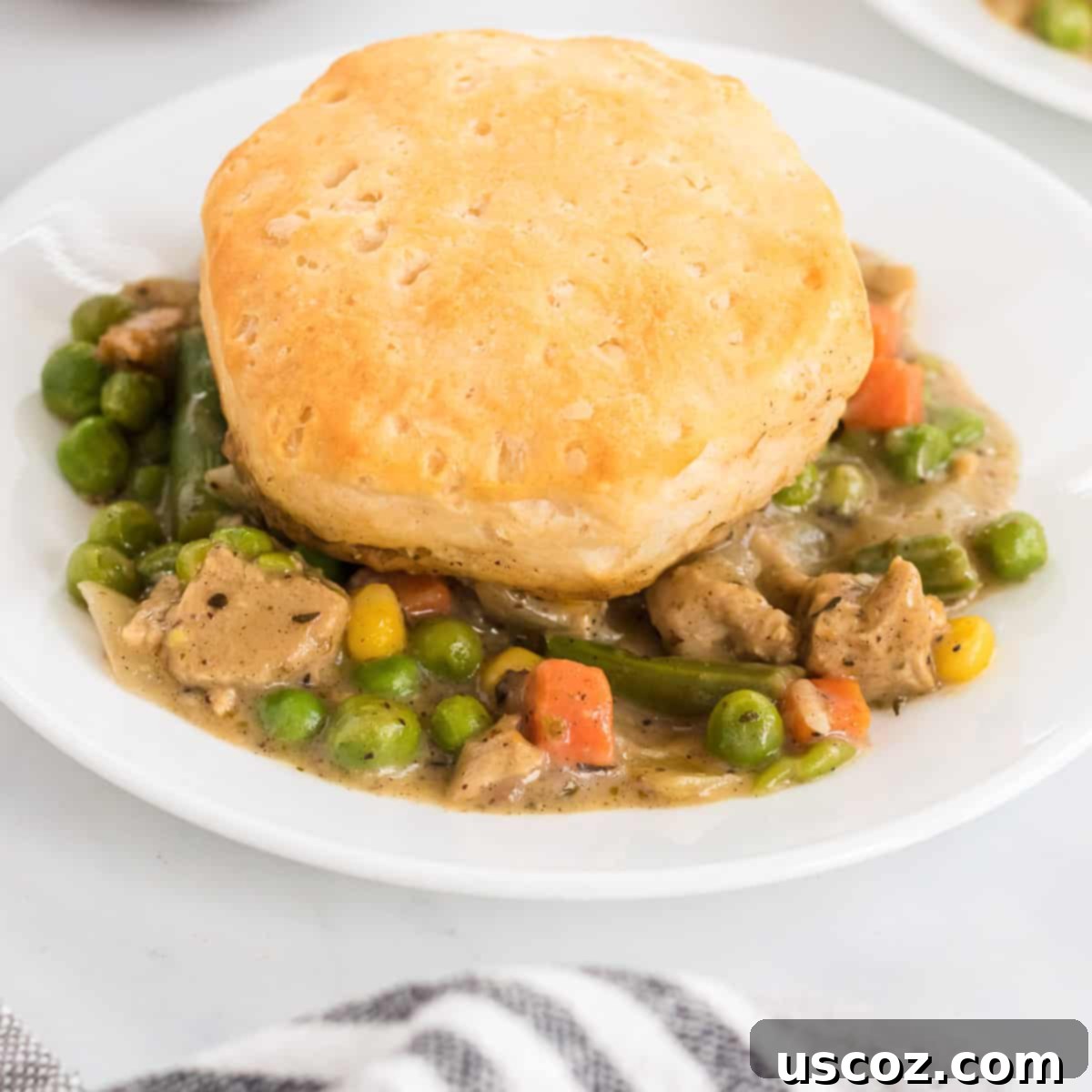 Garden Harvest Pie 13 A close-up shot of a single serving of veggie pot pie, topped with a biscuit, on a white plate, highlighting the creamy texture and fresh ingredients.