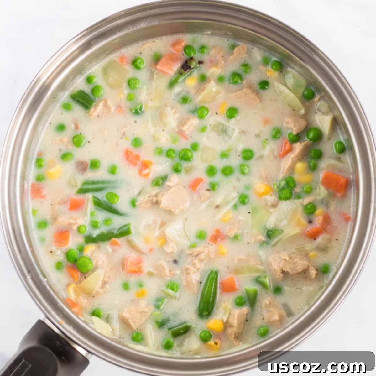 Garden Harvest Pie 6 Cream of mushroom soup, vegetable broth, and milk are being added to the sautéed onions, garlic, and frozen mixed vegetables in a large skillet to create the pot pie filling.