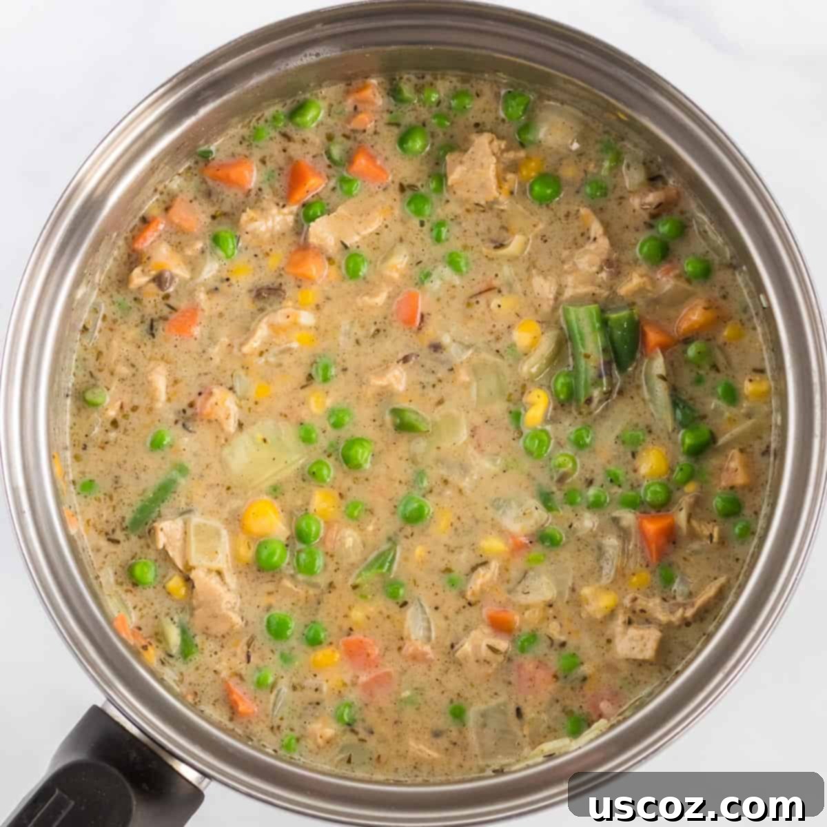 Garden Harvest Pie 7 The creamy veggie pot pie filling, rich with vegetables, meatless chick'n, and melted cheddar cheese, simmers in a sauce pan, ready for baking.