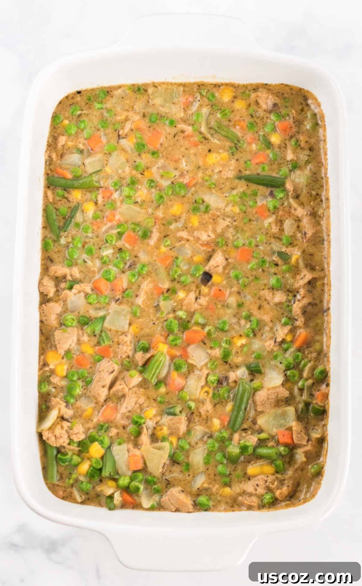 Garden Harvest Pie 9 The hot and bubbly veggie pot pie filling is scooped into a white casserole dish, ready to be topped with freshly baked biscuits.
