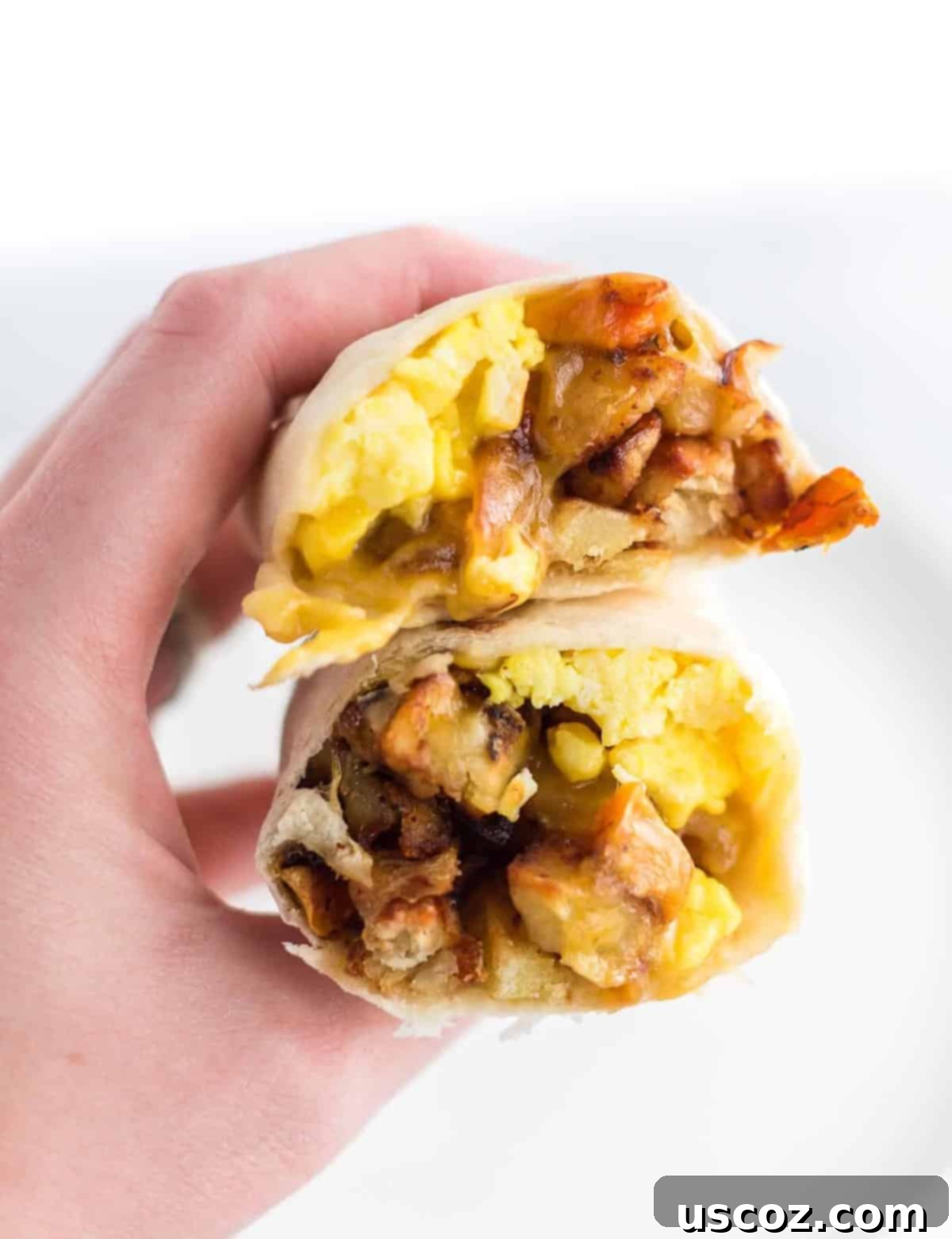 Your New Favorite Breakfast Burrito 2 A hand holding a breakfast burrito cut open, revealing fluffy eggs, crispy hash, and melted cheese