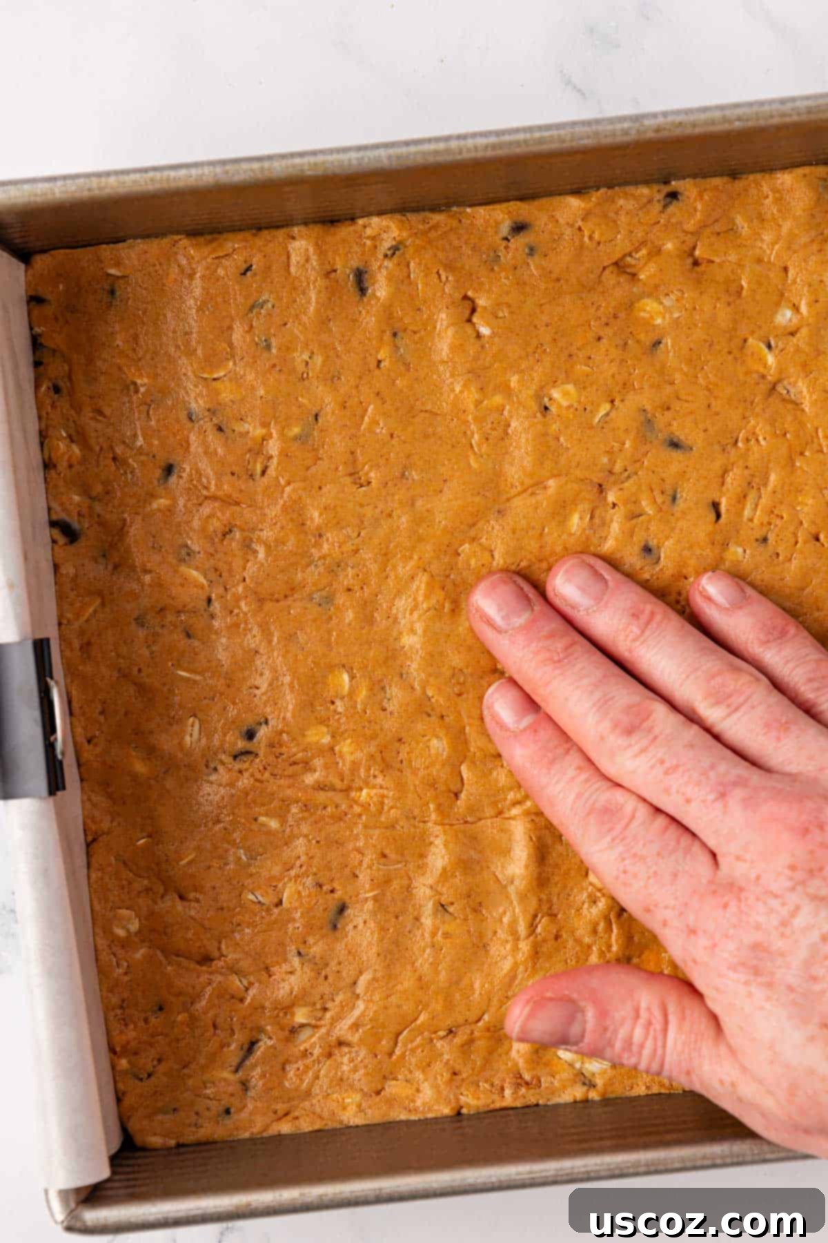 PB & Chocolate Chip Protein Bars 8 Hand pressing protein bar batter firmly into a baking dish.