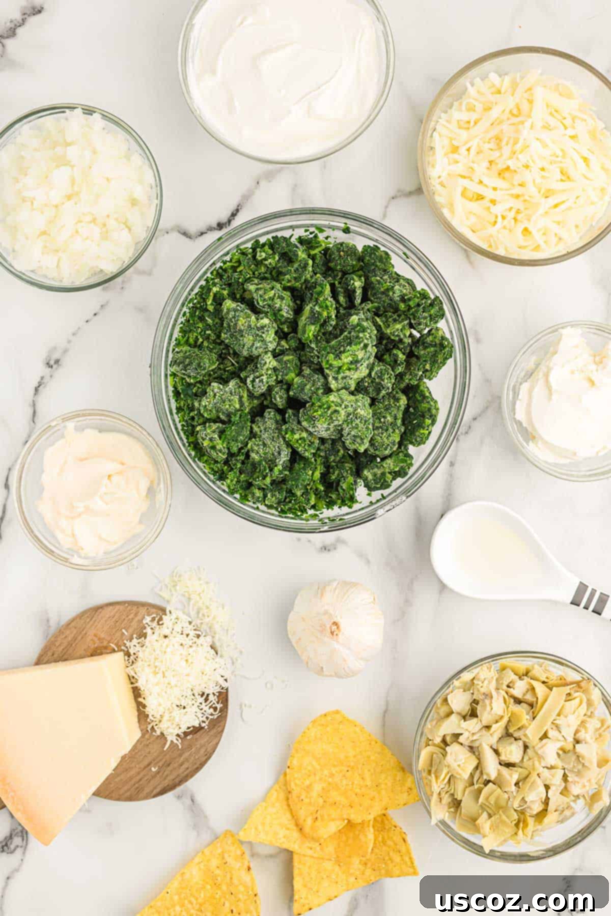The Ultimate Baked Spinach Artichoke Dip 4 A flat lay of all fresh and packaged ingredients for spinach artichoke dip, including onion, garlic, cheeses, and cans of artichoke hearts