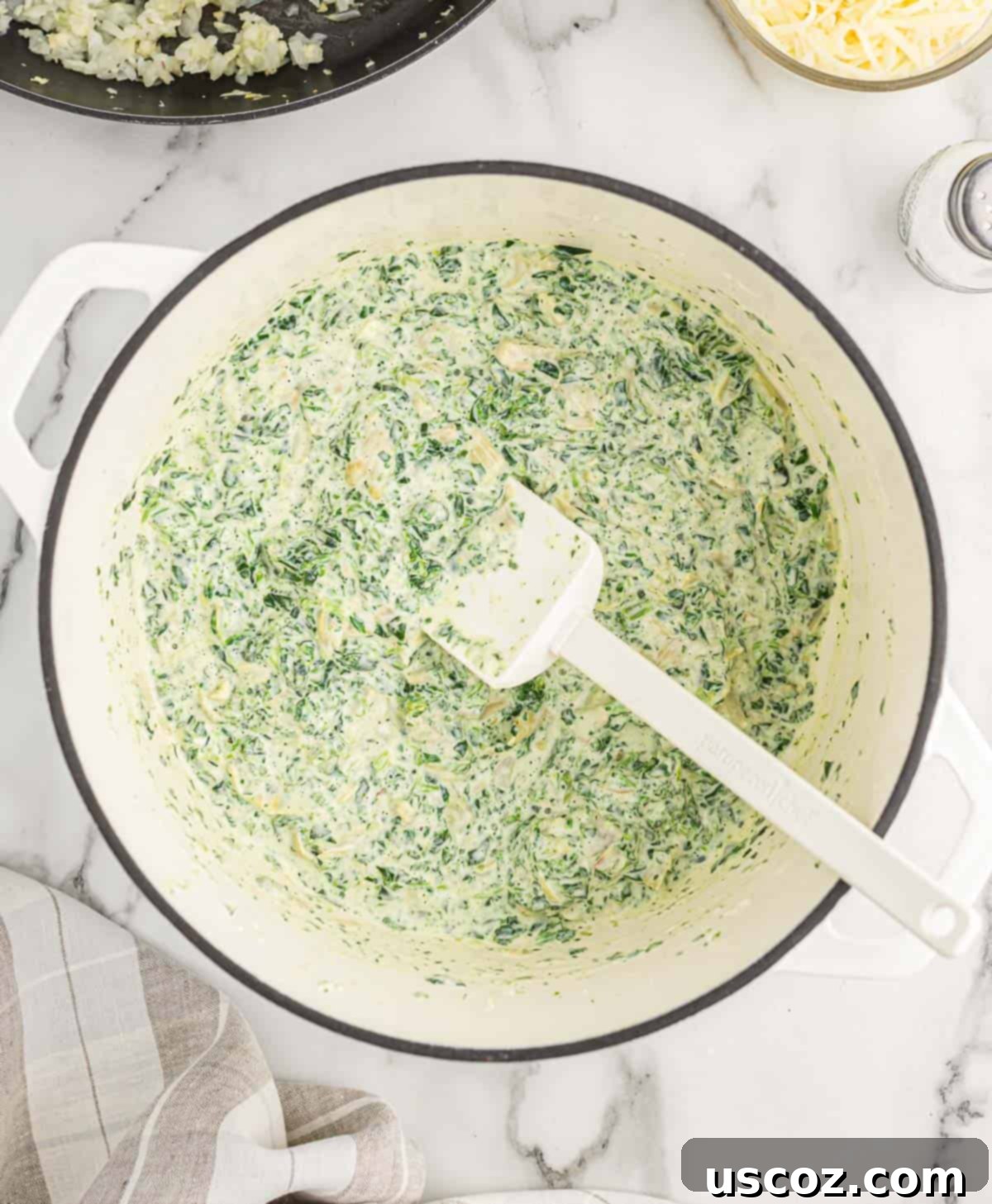 The Ultimate Baked Spinach Artichoke Dip 7 Creamy spinach artichoke dip melting and combining in a Dutch oven, creating a smooth base