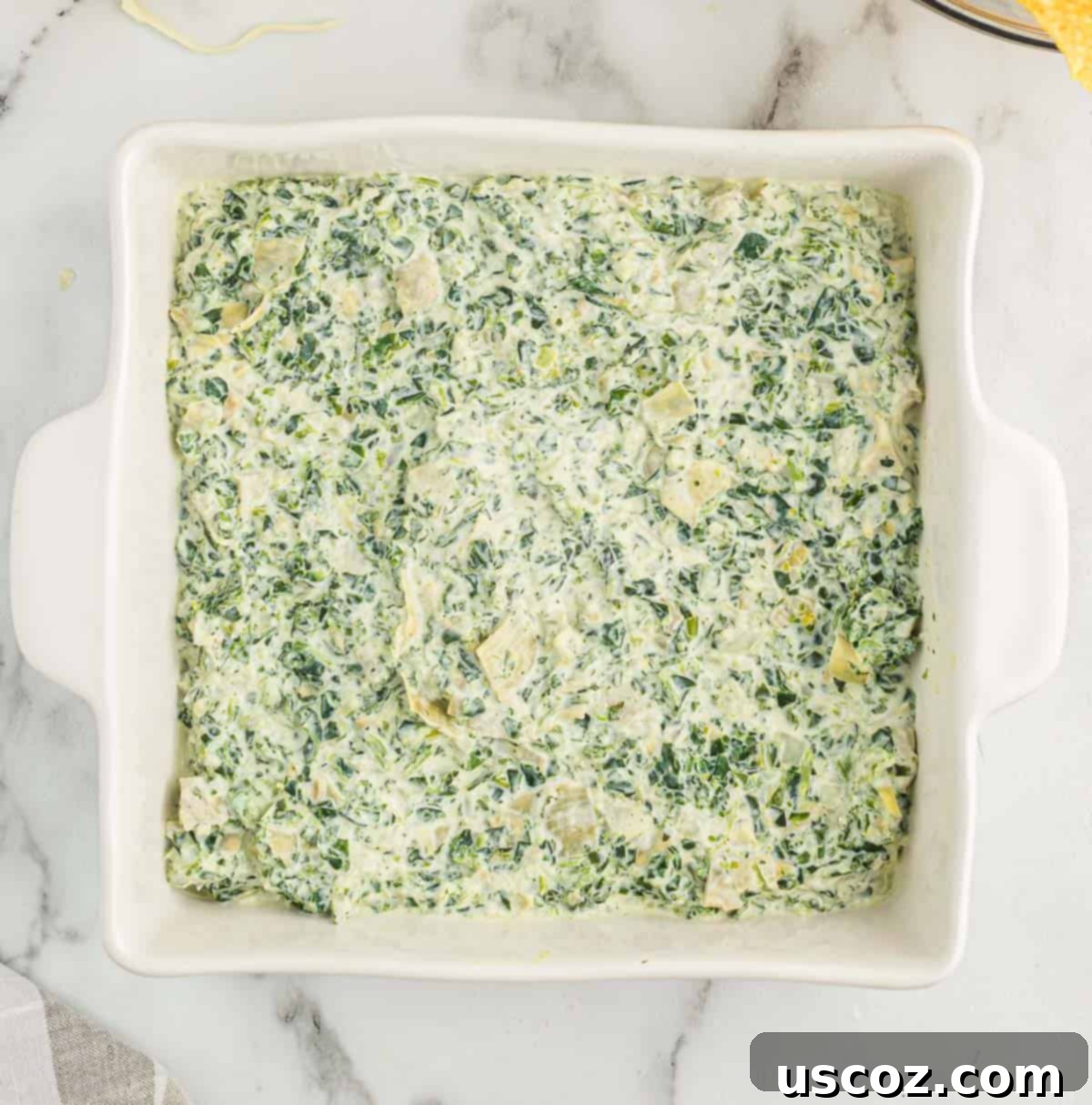The Ultimate Baked Spinach Artichoke Dip 8 Spinach artichoke dip evenly spread in a white baking dish before going into the oven