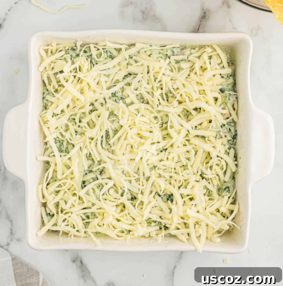The Ultimate Baked Spinach Artichoke Dip 9 Spinach artichoke dip in a white baking dish, topped generously with shredded mozzarella cheese