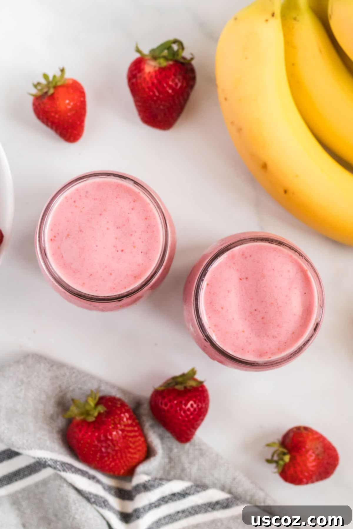 Sweet Strawberry Banana Bliss 7 smoothies in glass jars from an overhead view surrounded by strawberries and bananas
